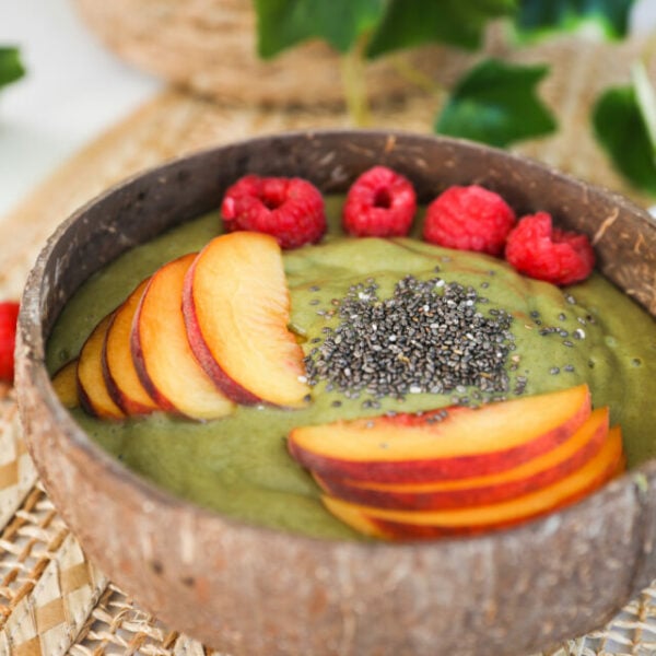 Perspective shot of a green smoothie bowl topped with chopped peached, berries and seeds.