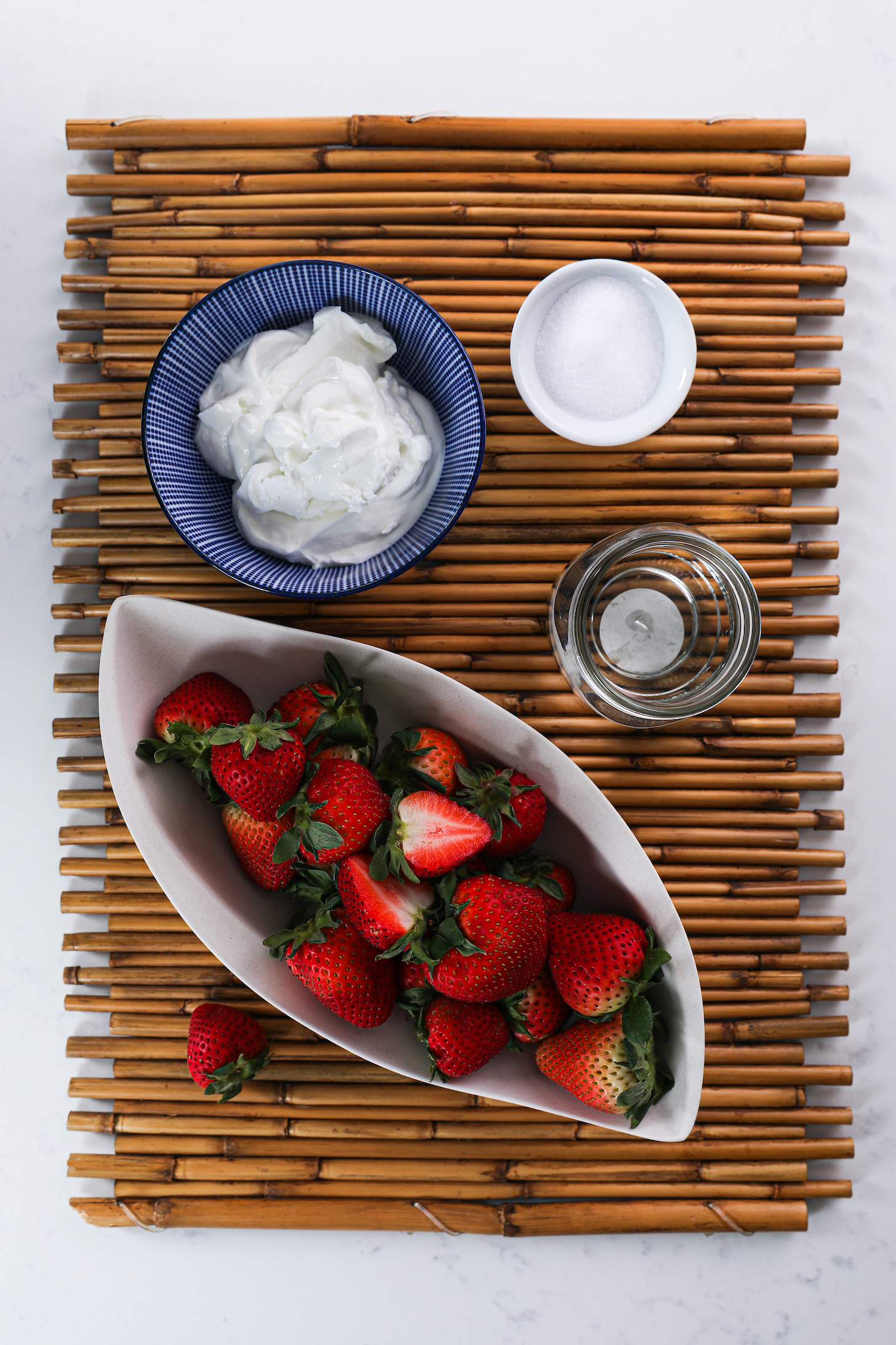 A collection of food ingredients like fresh strawberries, yogurt and water on a bamboo place mat.