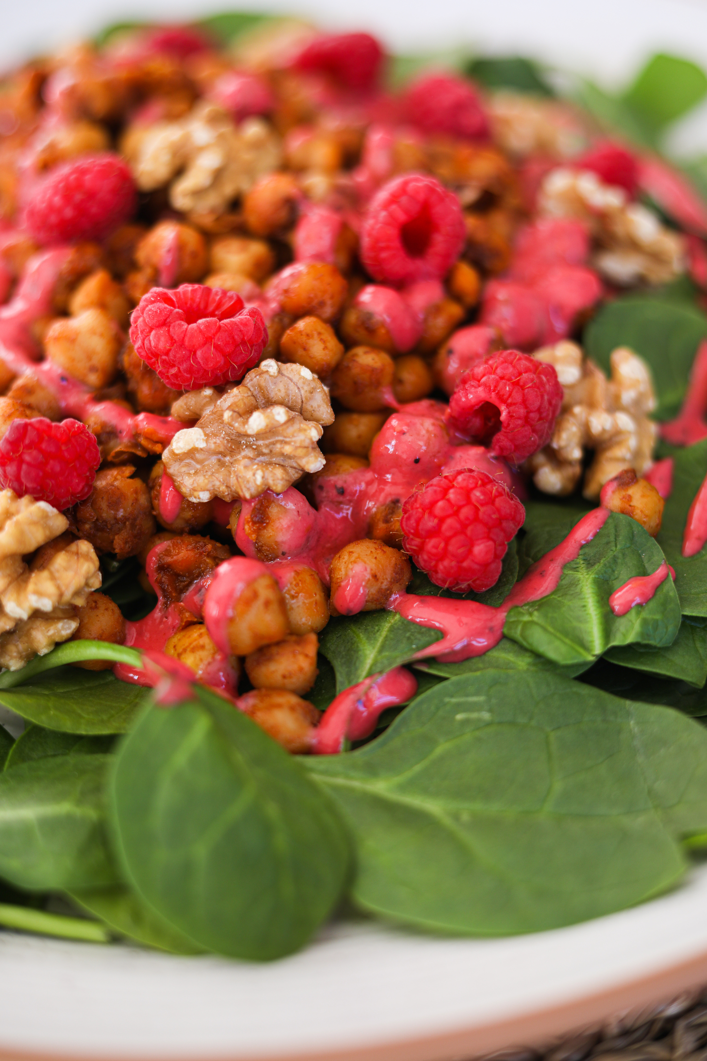 A close up image of chickpeas on a bed of spinach topped with raspberries, walnuts and a red dressing.
