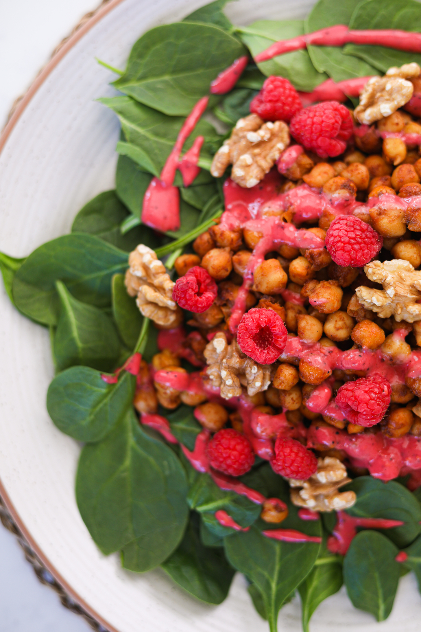 View of half a plate of chickpeas on a bed of spinach topped with raspberries, walnuts and a red dressing.