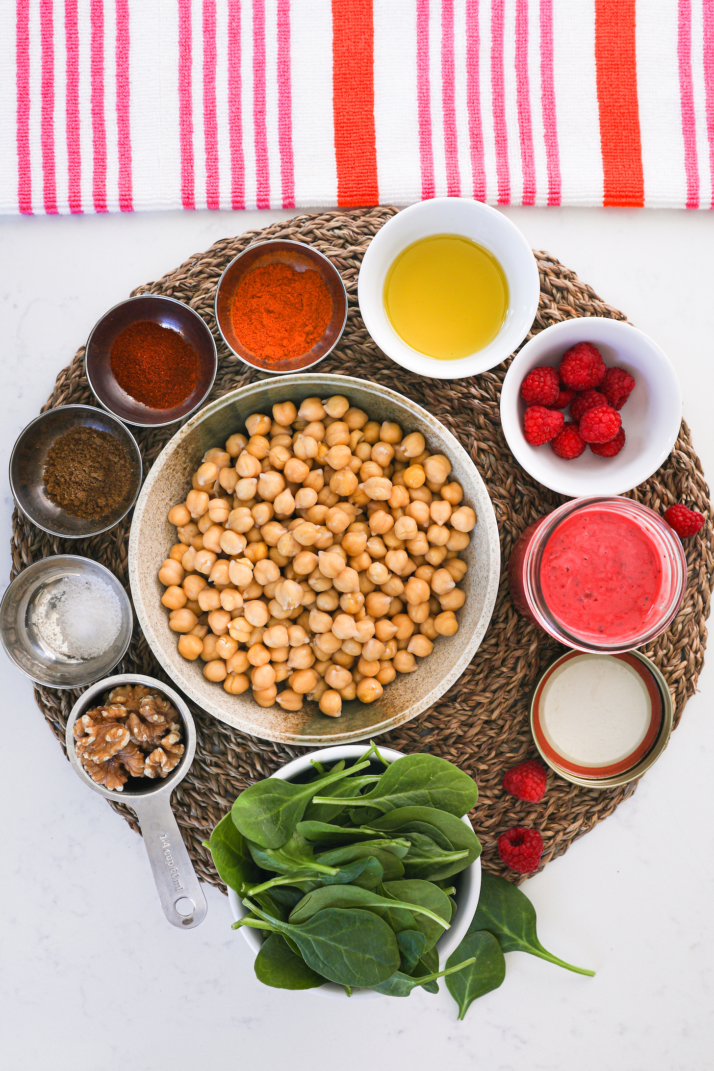 A coloourful display of food ingredients inlcuding chickpeas, spices, spinach and a red sauce on a straw mat.