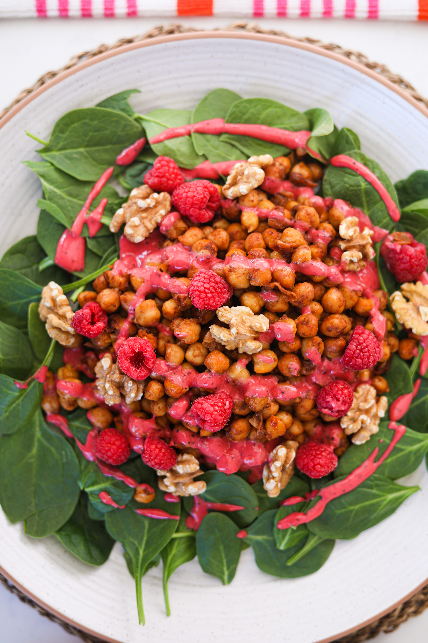 Flat lay of a plate of chickpeas on a bed of spinach topped with raspberries, walnuts and a red dressing.