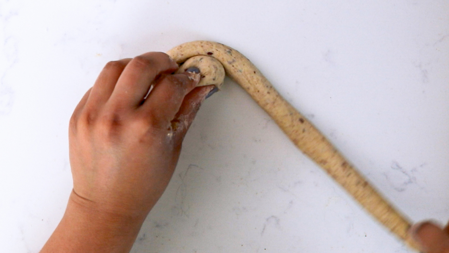 Hands holding a long worm-shaped dough and creating a swirl.