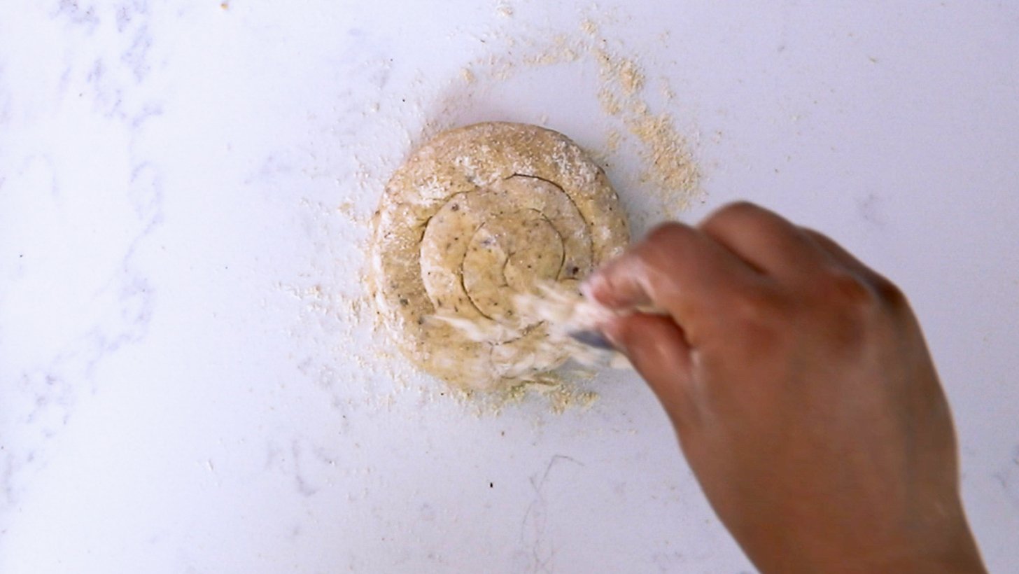 A hand sprinkling flour on a round flat dough.