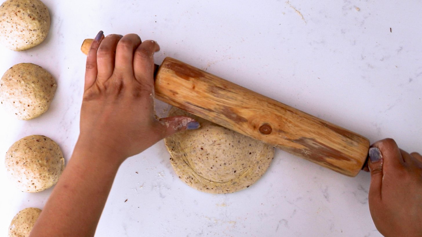 Hands holding a rolling pin and rolling out dough.