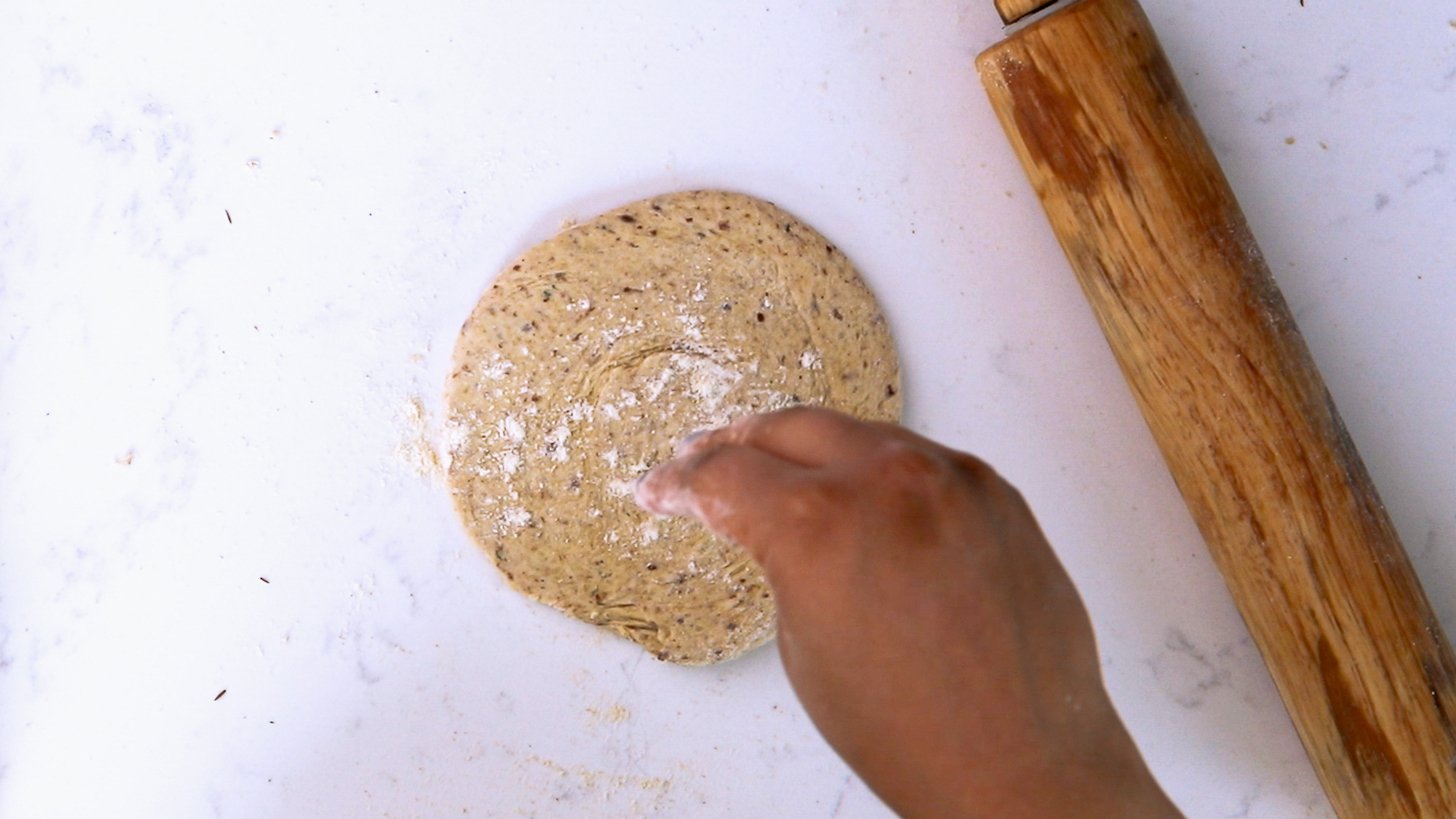 Hand sprinkling flour on a circular-shaped rolled-out dough.