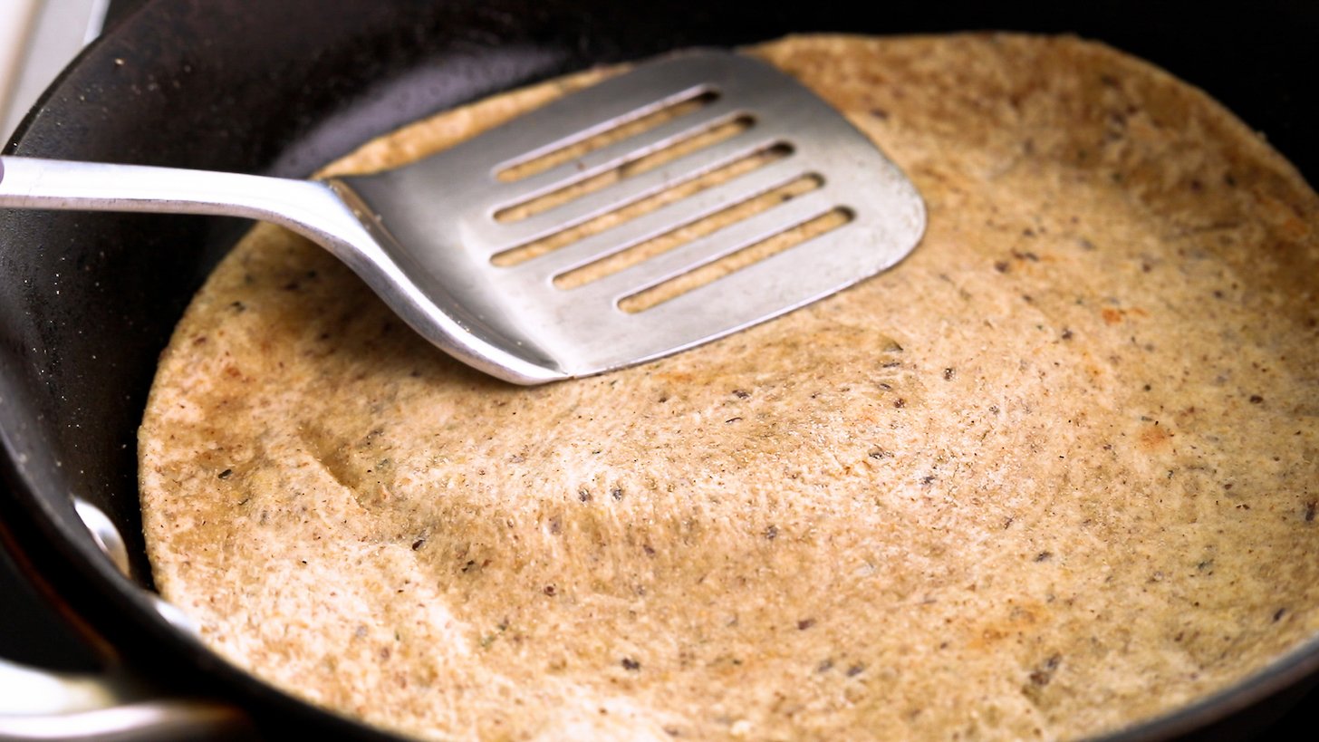 A metal spatula pressing flatbread in a pan.