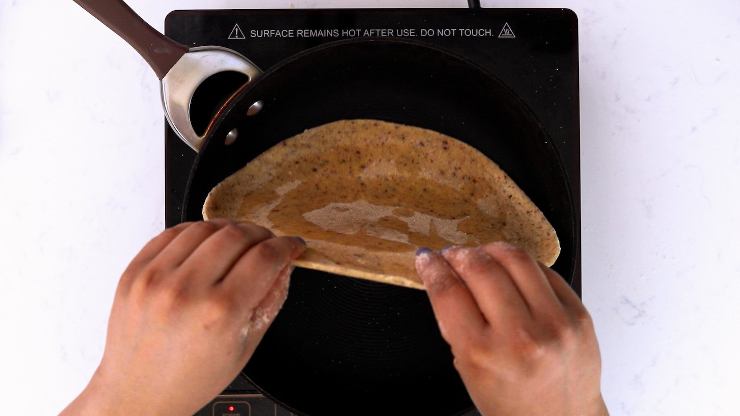 Hands holding uncooked flatbread with oil and flipping it over in a pan.