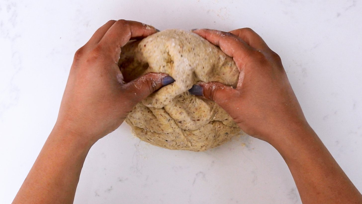 Hands kneading dough on a white surface.