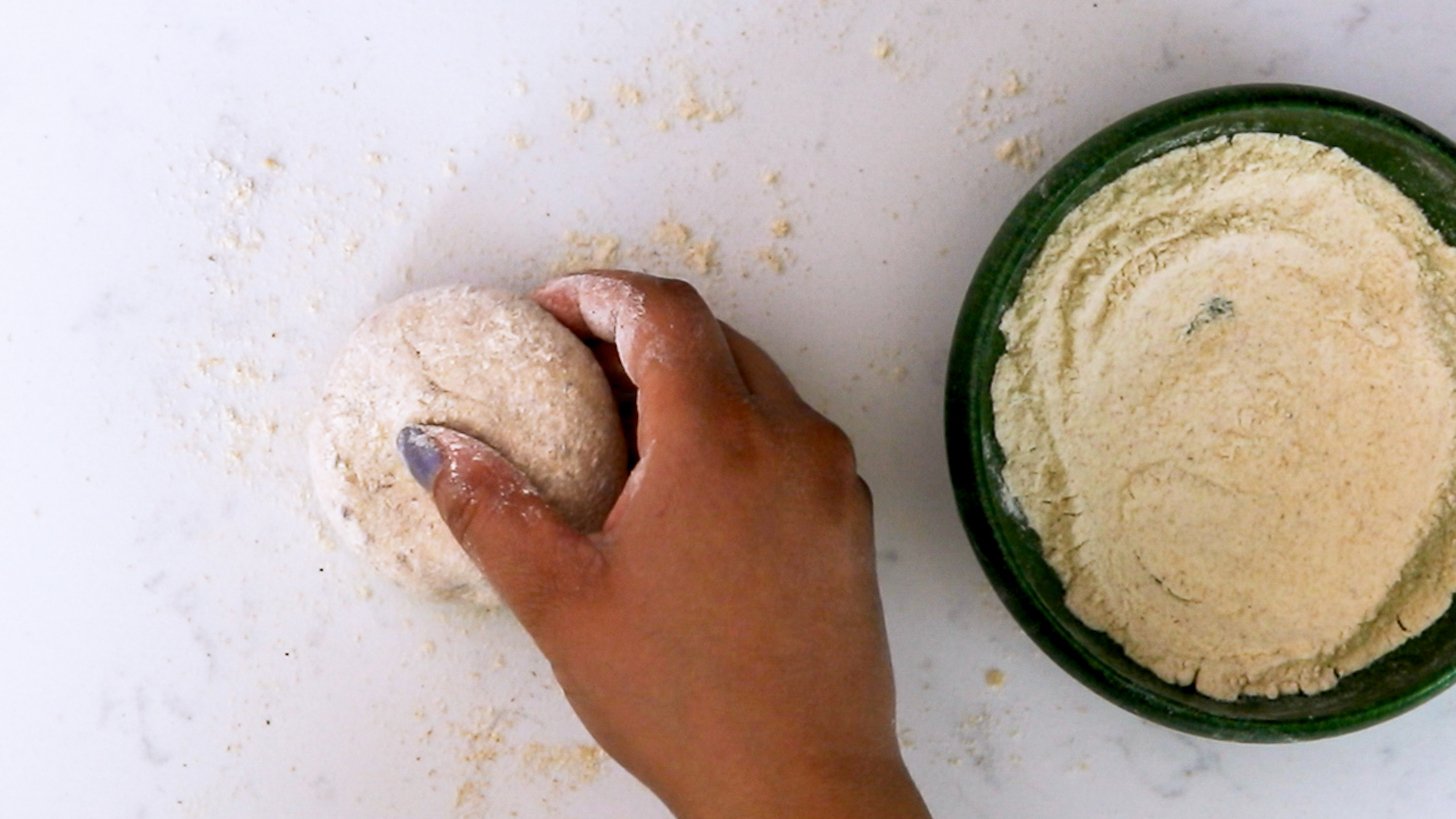 Hand holding a ball of dough coated in flour with a bowl of flour close by.