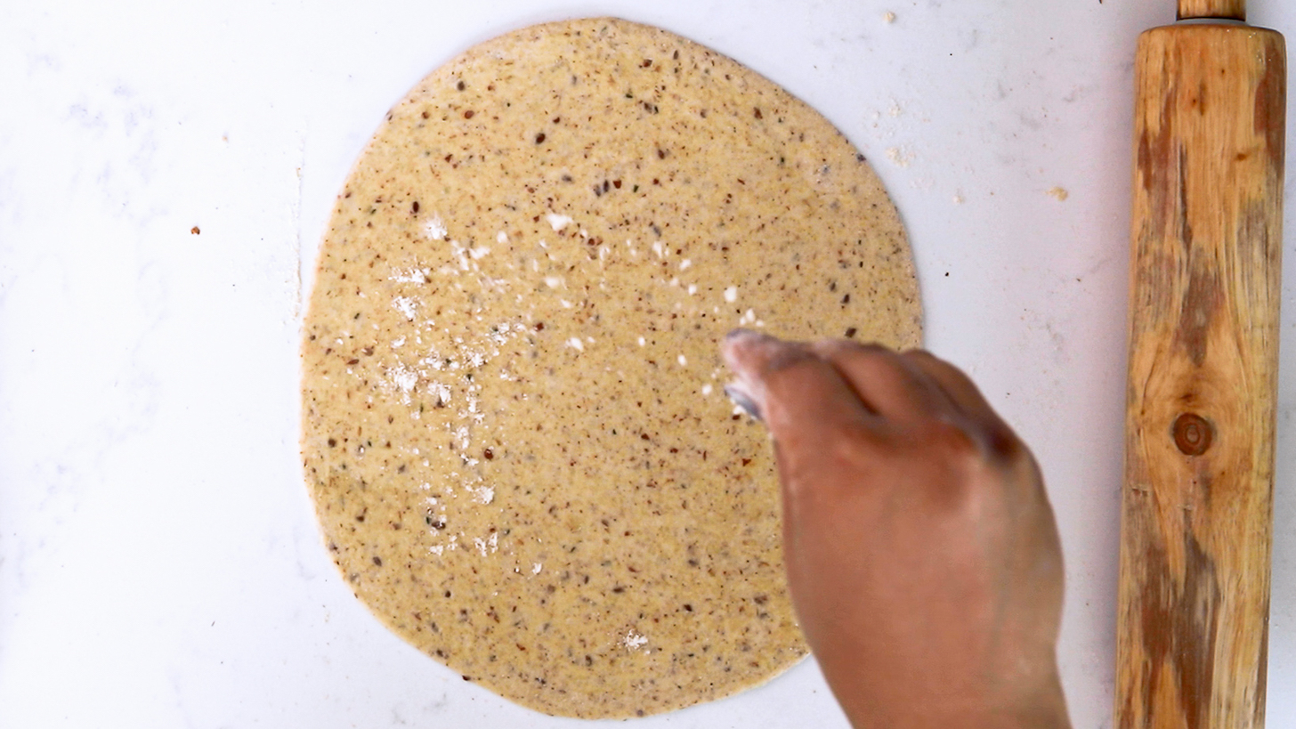 Hand sprinkling flour on a circular rolled-out dough.