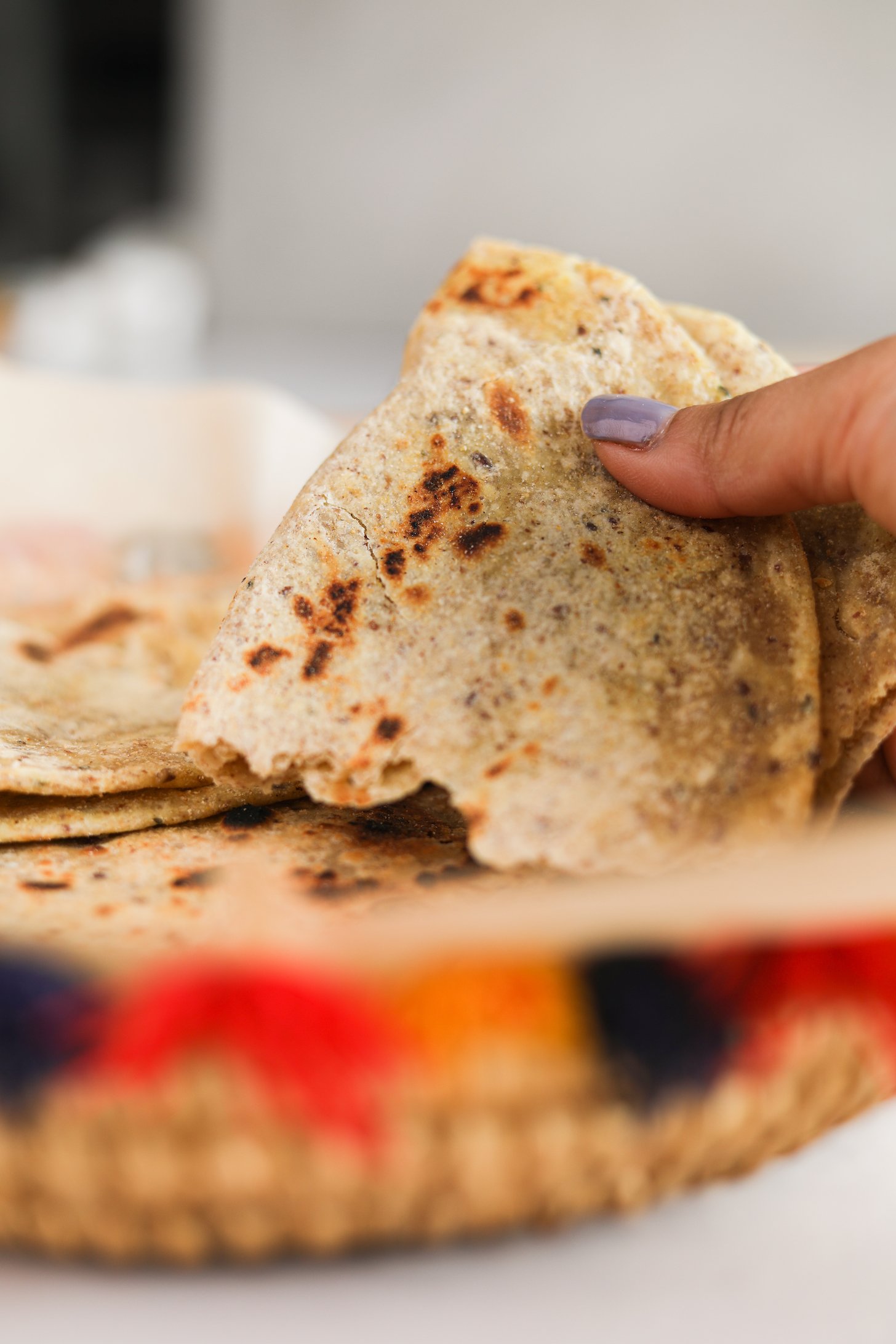 A hand holding a folded half of Indian flatbread - paratha in the colourful basket.