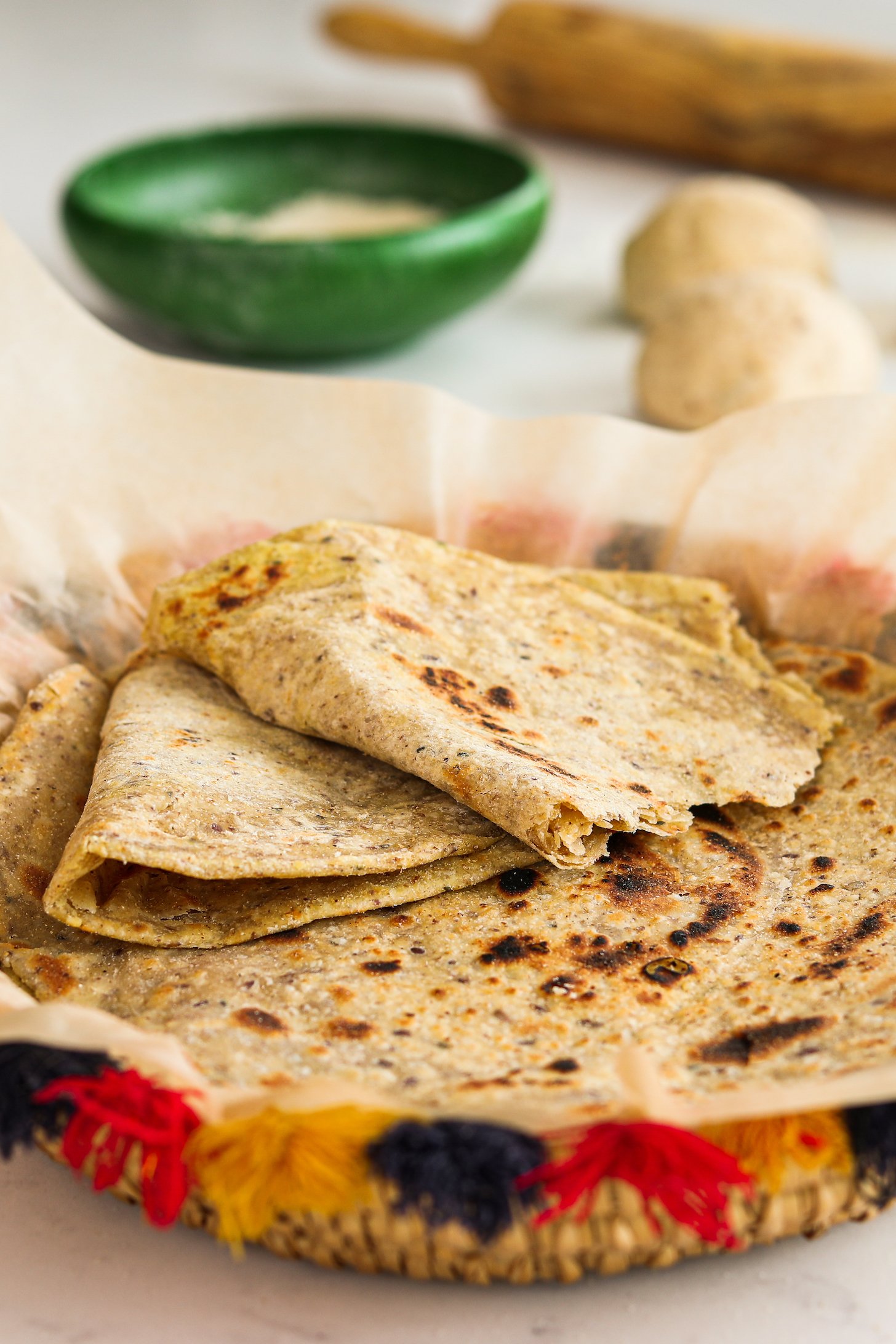 A decorative basket of flatbread (paratha) - with one ripped in half stacked on top of one another.