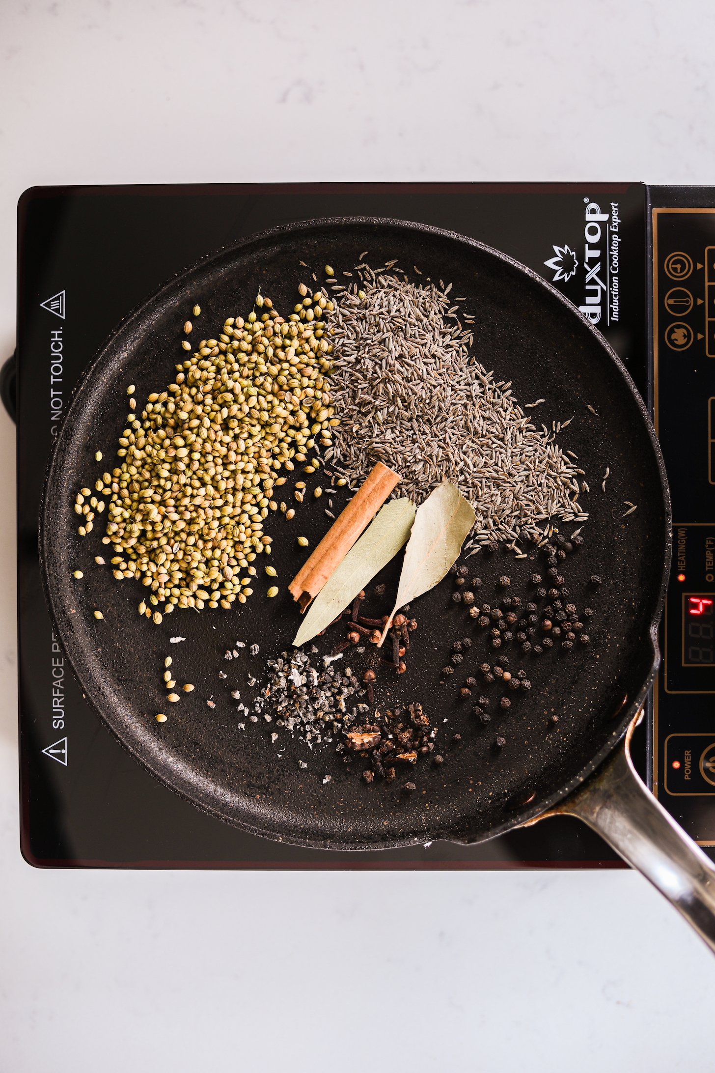 Whole spices on a tava (Indian girdle) heating over a mobile stovetop.