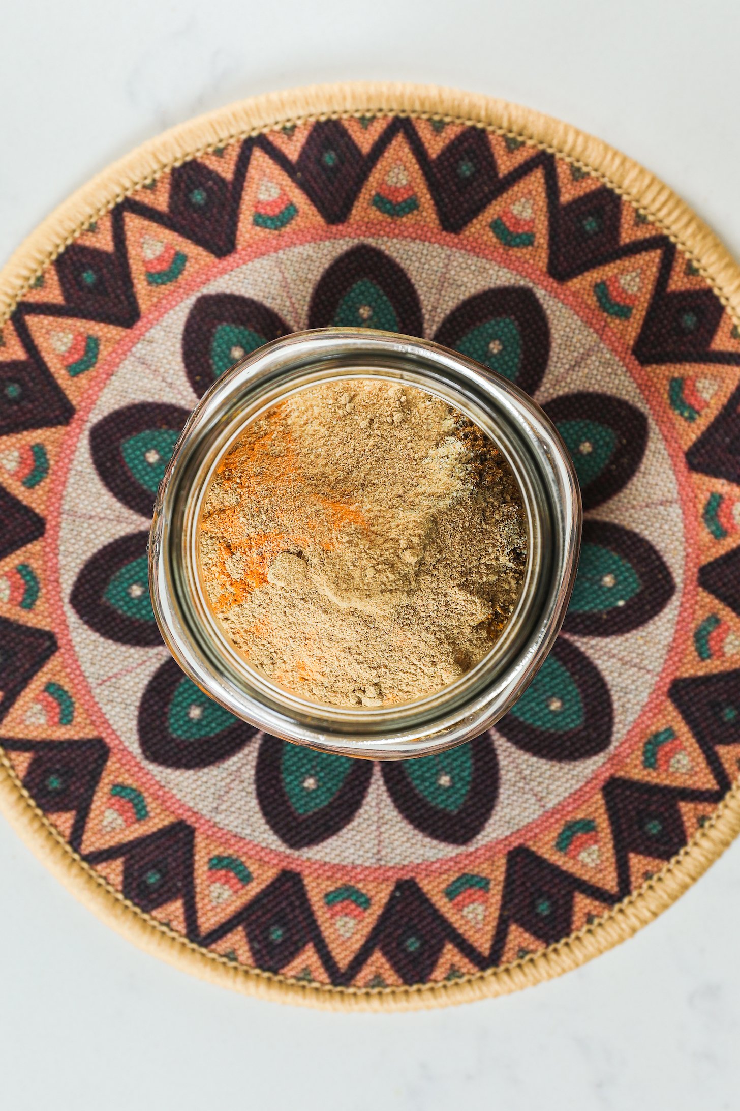Top view of a jar with ground spices on a patterned placemat.