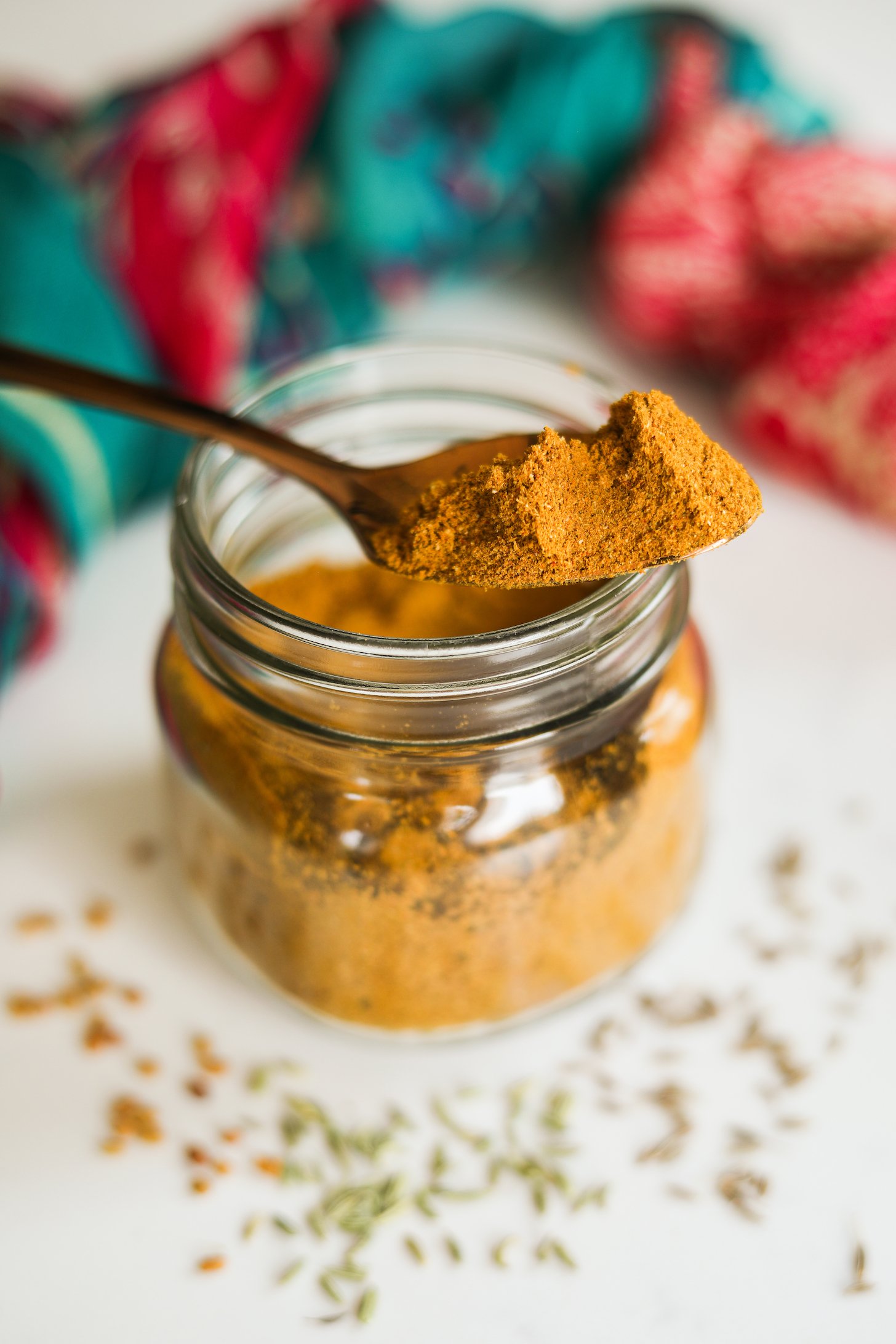 A heap-ful spoon of yellow spice powder sitting on a jar of ground spices with whole spices scattered close by.