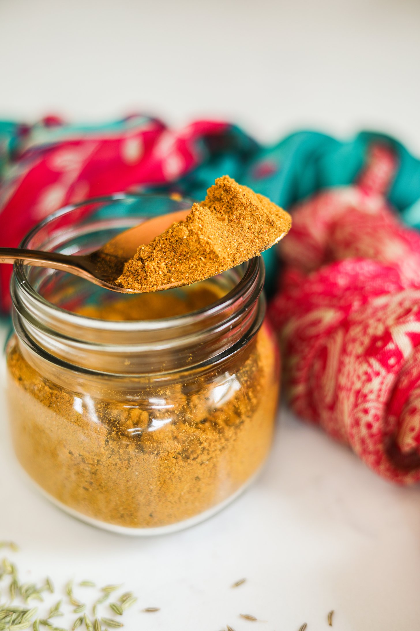 A heap-ful spoon of yellow spice powder sitting on a jar of ground spices.