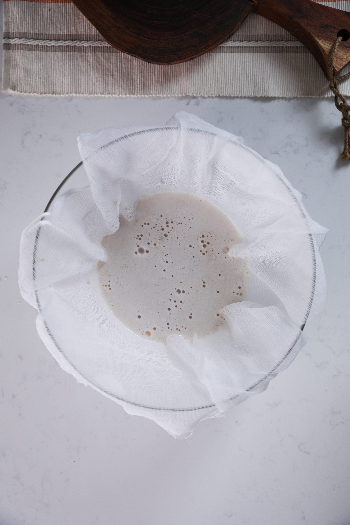 Overhead shot of a cheesecloth-lined bowl with milk in it.