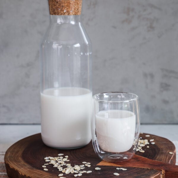 A bottle and glass of milk on a wooden board with rolled oats sprinkled all around.