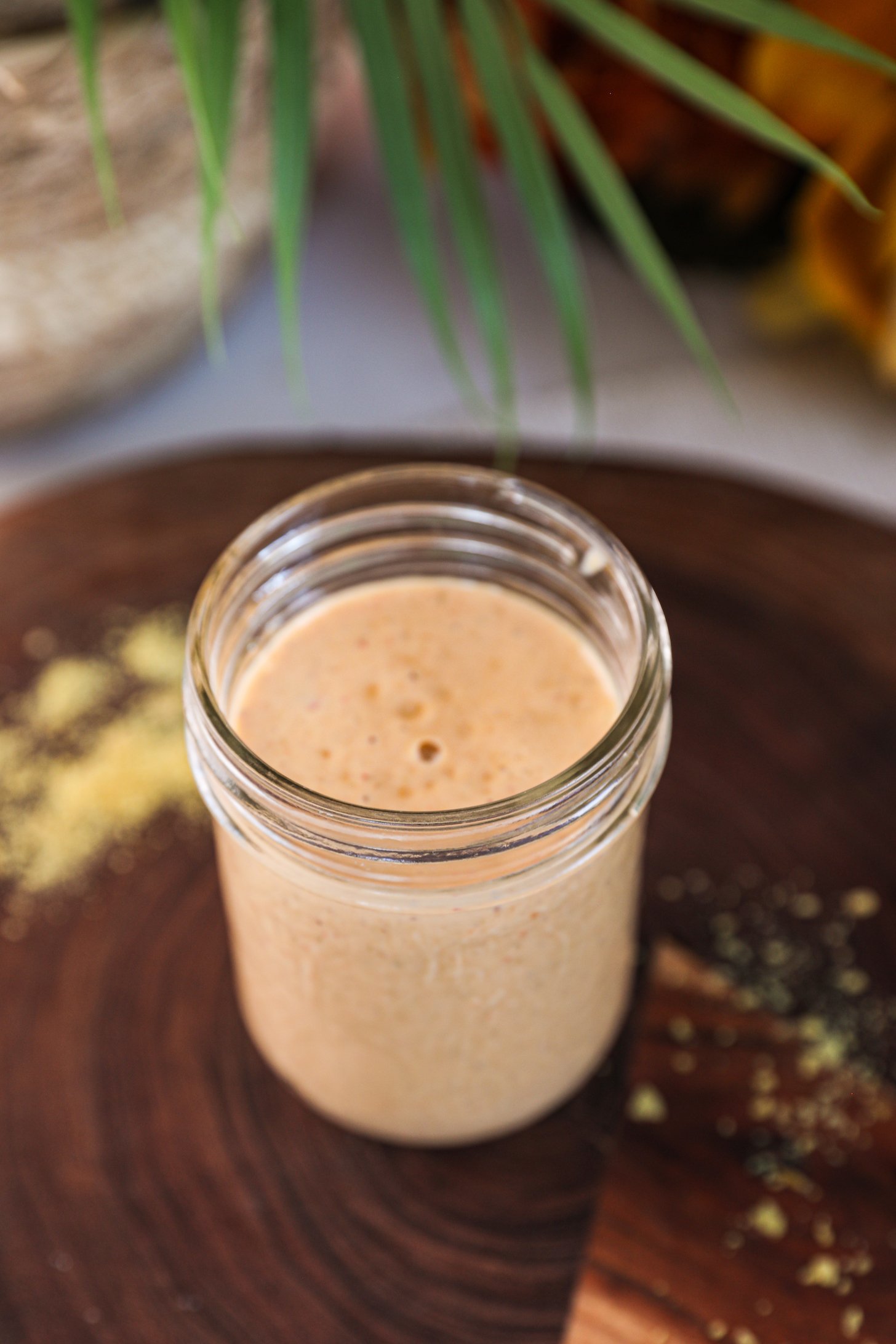 Perspective view of a mason jar of yellow dressing with a plant in the background.