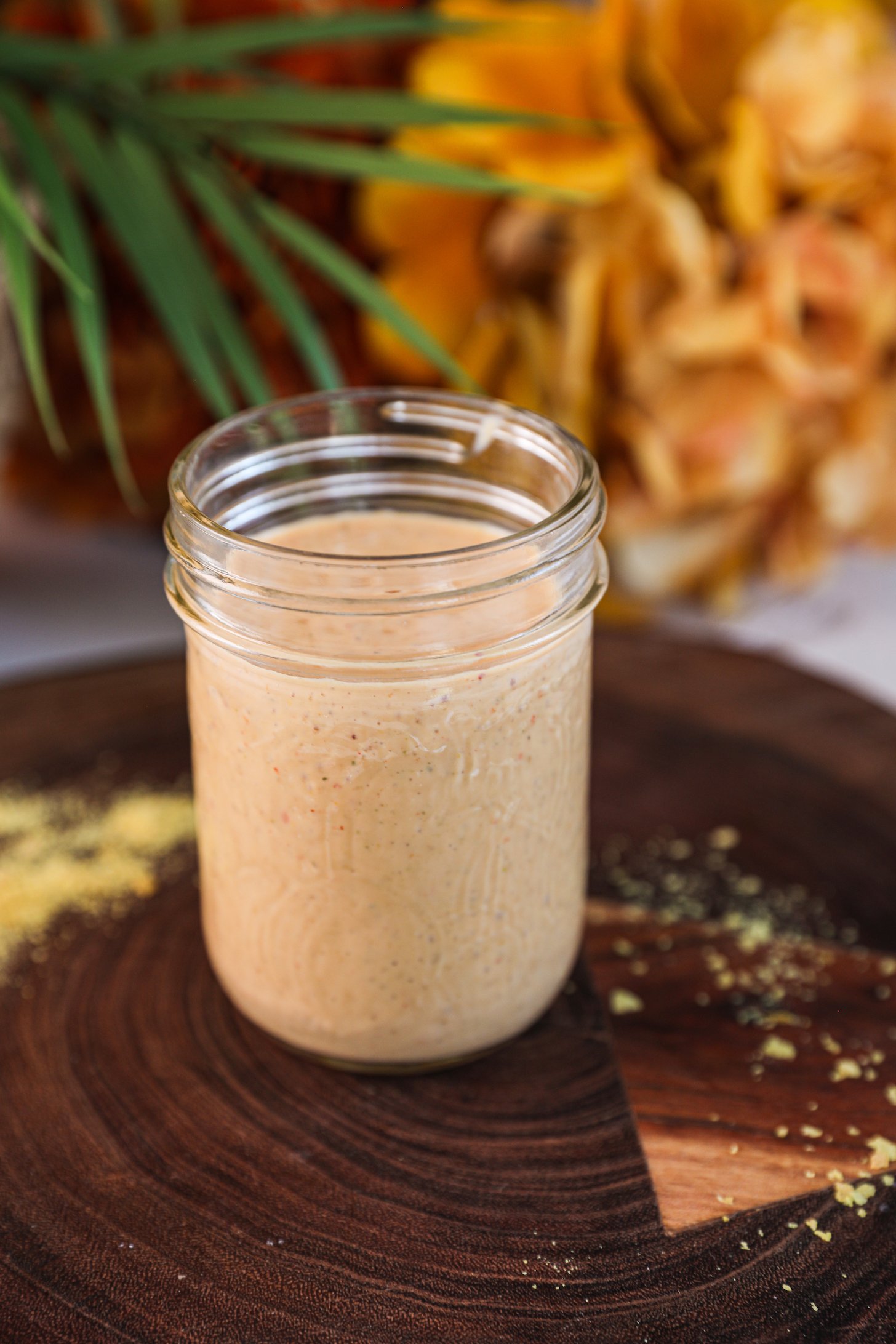 Perspective view of a mason jar of yellow dressing with plant and flowers in the background.