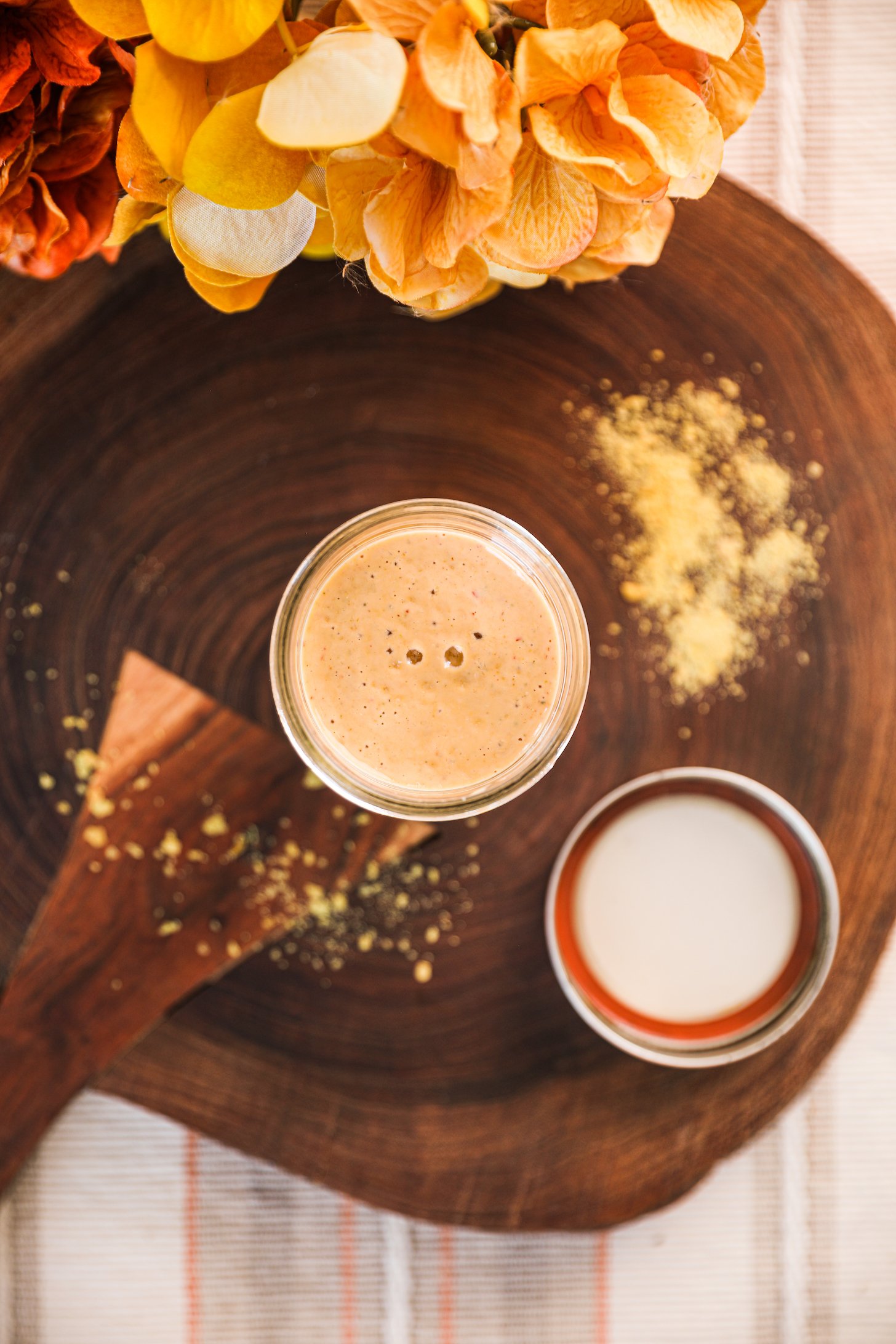 Top view of a mason jar of yellow sauce on a wooden board with sprinkles of a yellow powder.