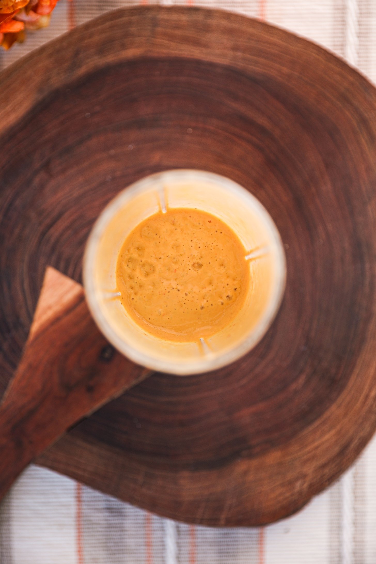 Overhead view of a glass of yellow dressing on a wooden board.