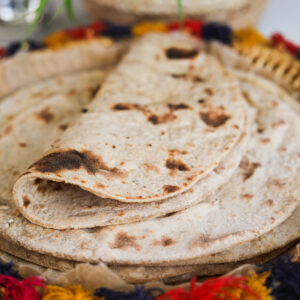 A folded roti on a pile of rotis on a decorative plate.