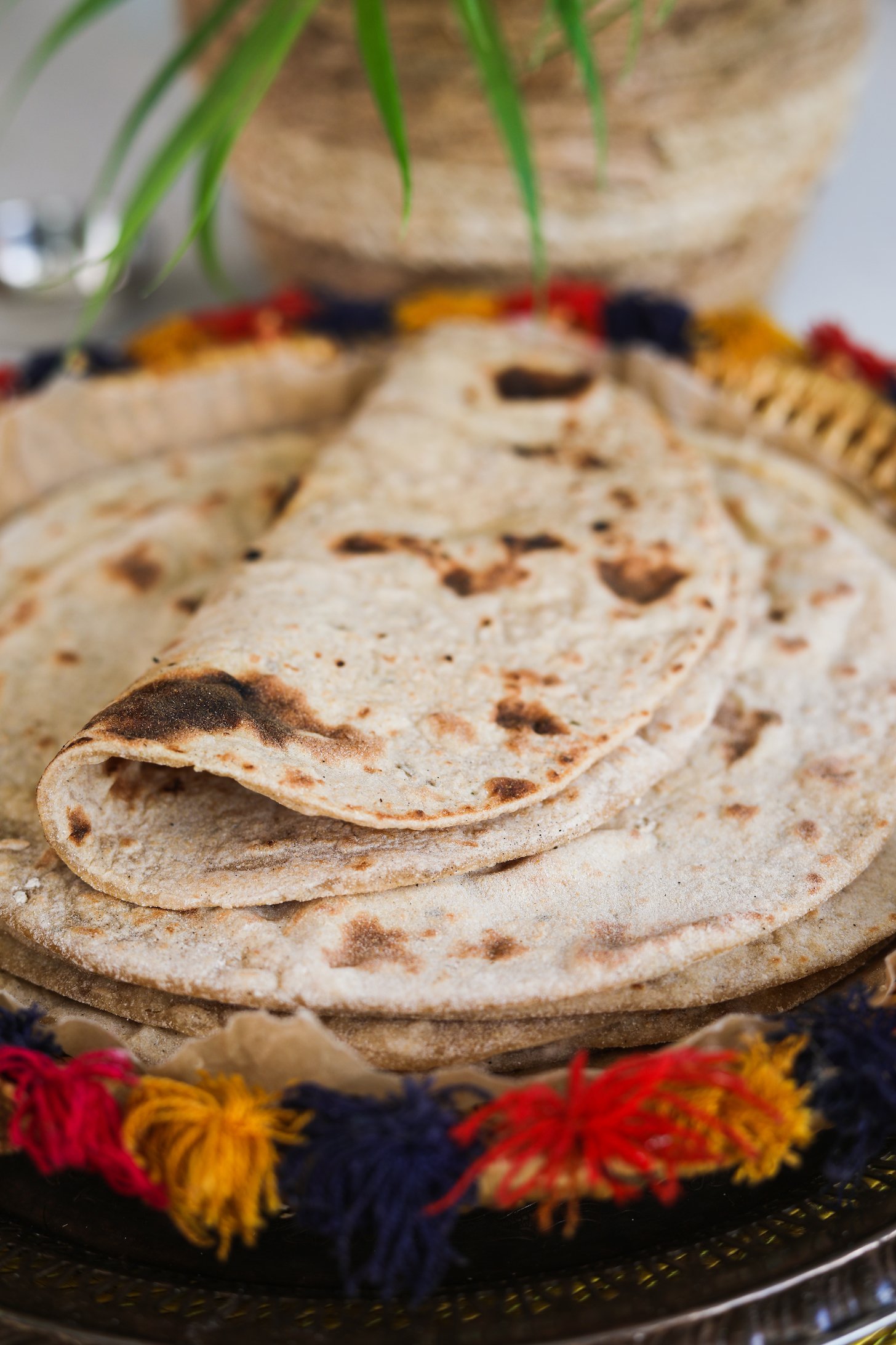 A folded roti on a pile of rotis on a decorative plate.