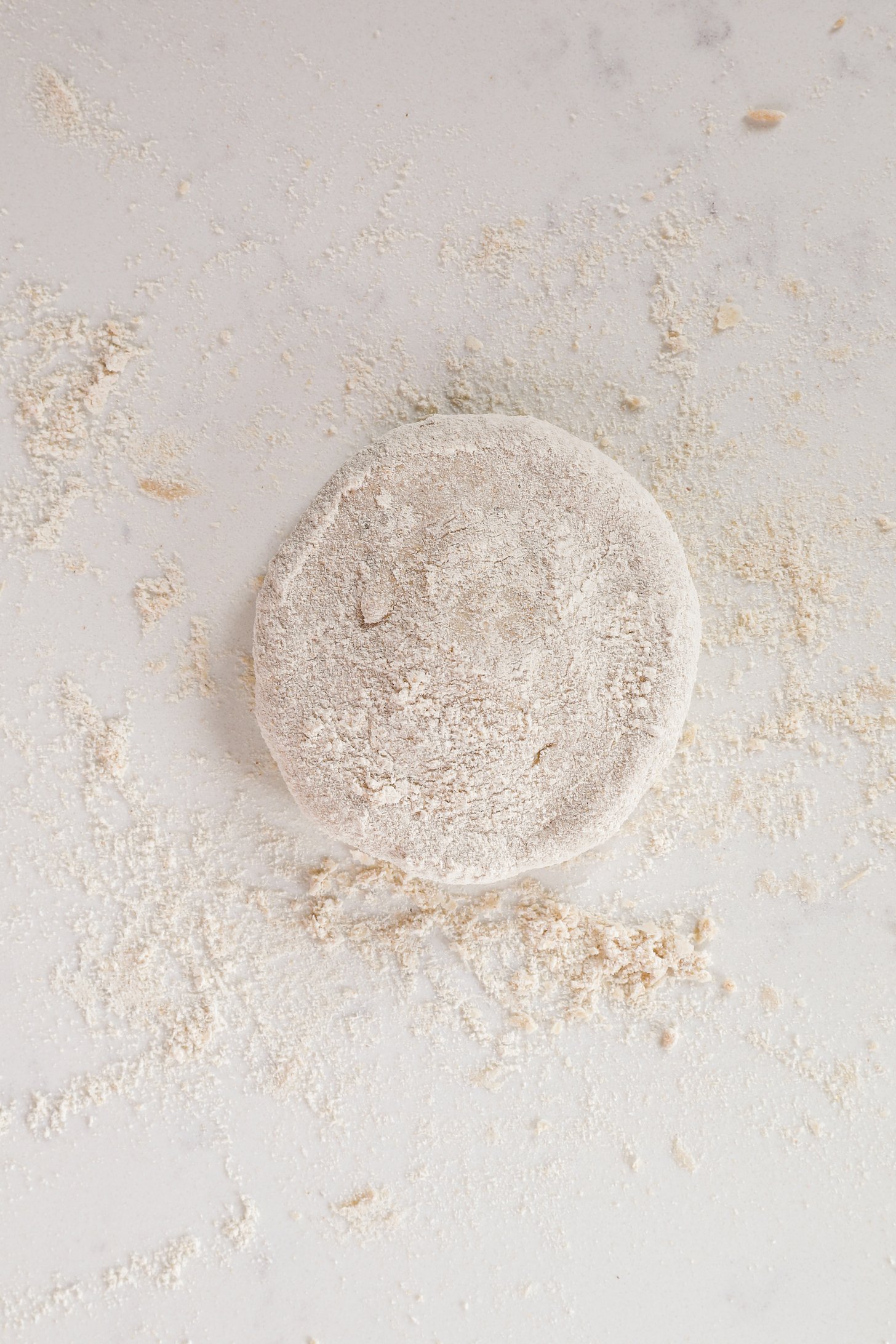 A thick flattened dough dusted with lots of flour on a flour-dusted worktop.