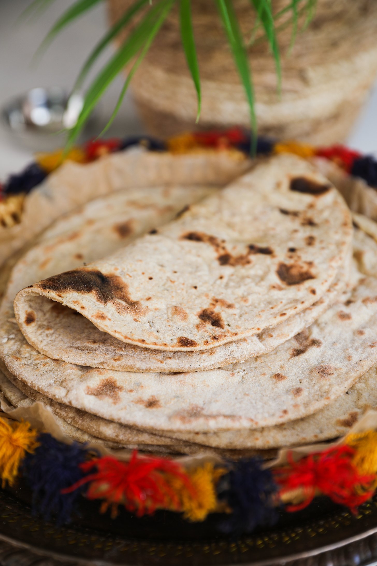 A perspective image of a folded roti on a pile of rotis on a decorative plate.