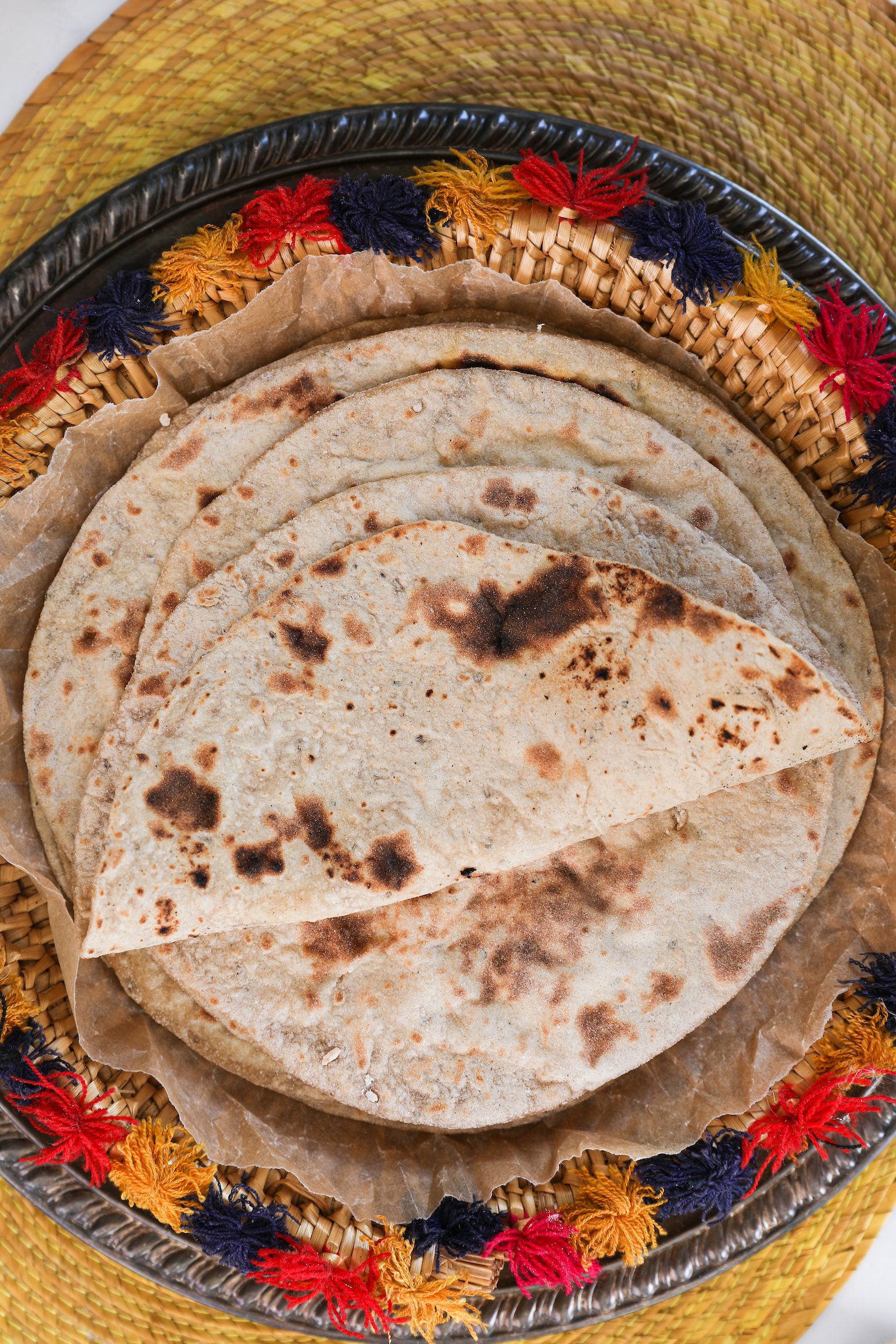 Flatlay of a pile of rotis with the top one folded styled on a decorative plate.