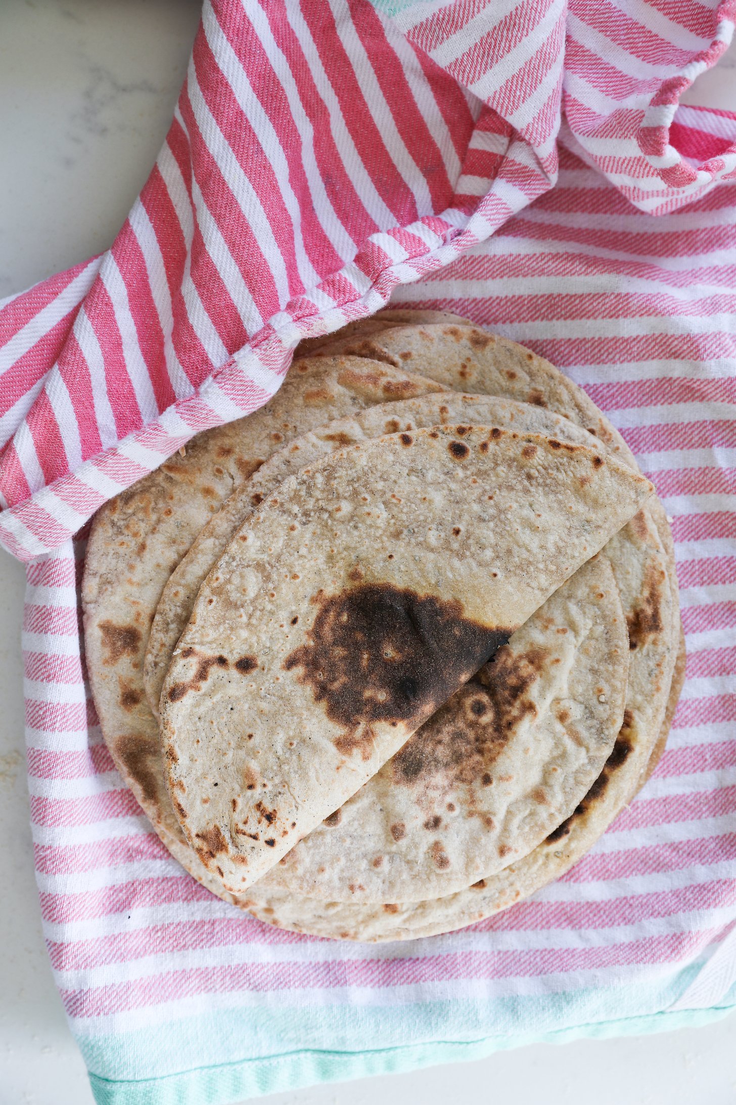A stack of rotis on a pink striped kitchen towel.