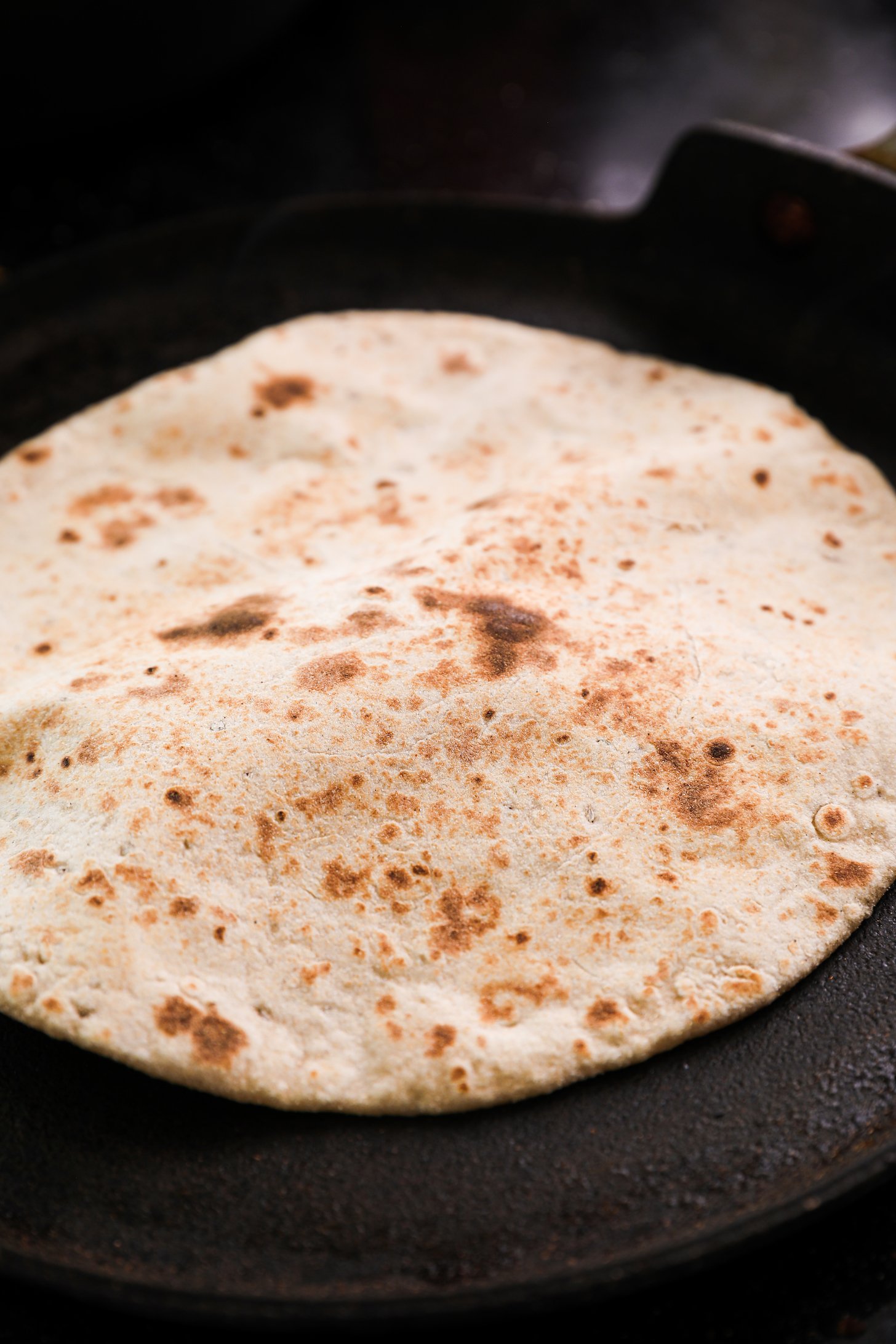 A roti cooking and puffing up on a flat pan.