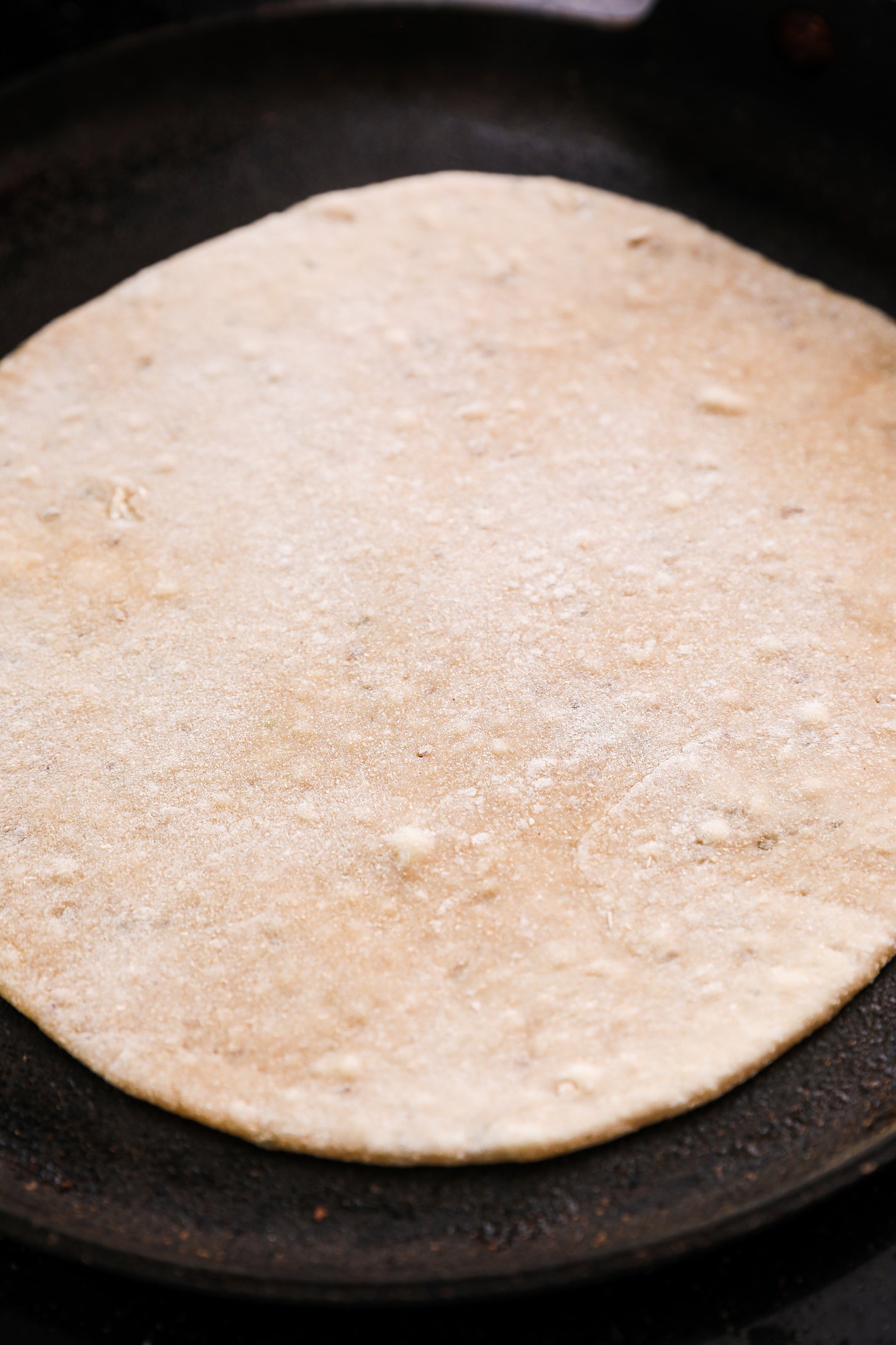 An uncooked roti on a flat pan.