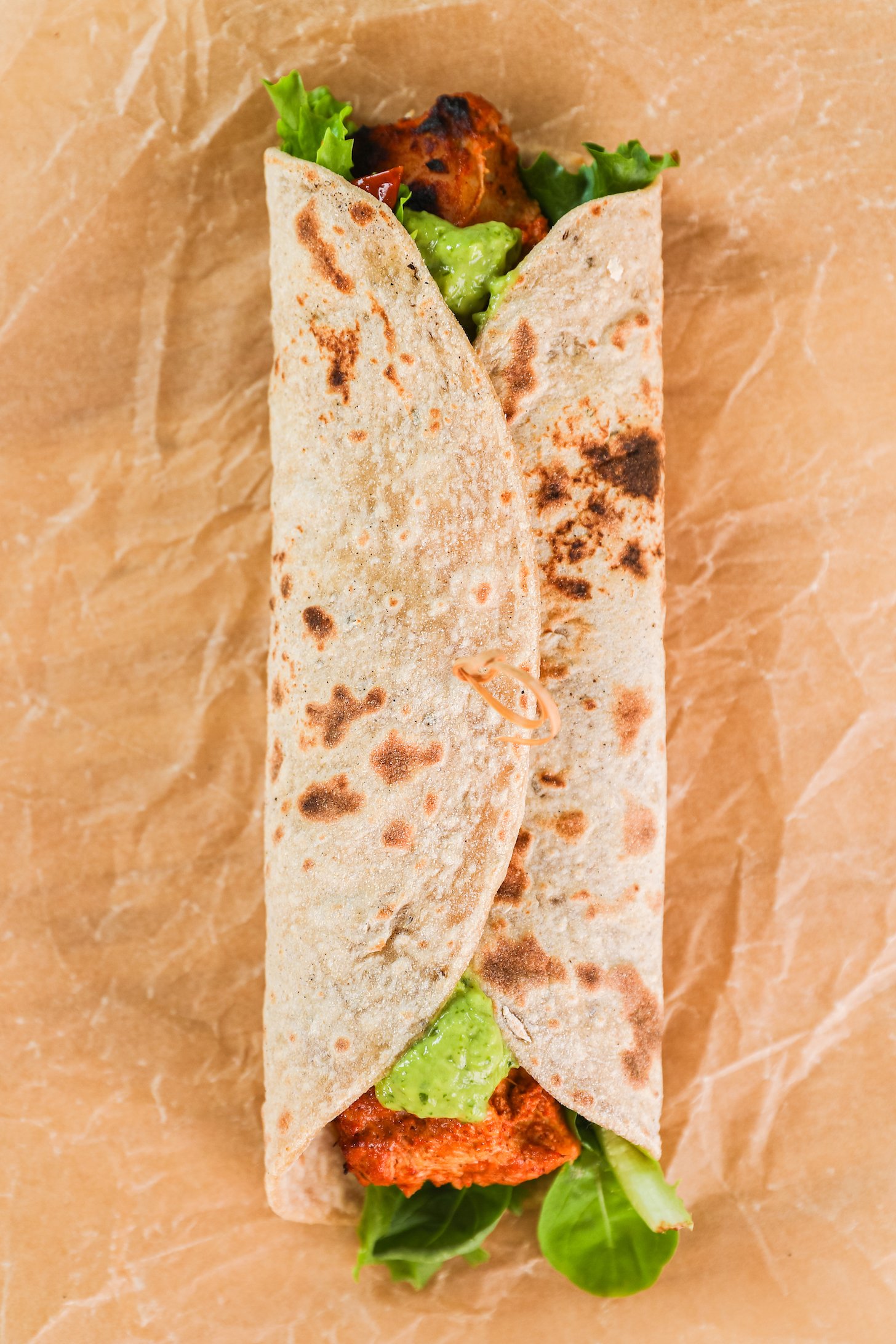 A roti wrap filled with chicken, green sauce and fresh salad greens.
