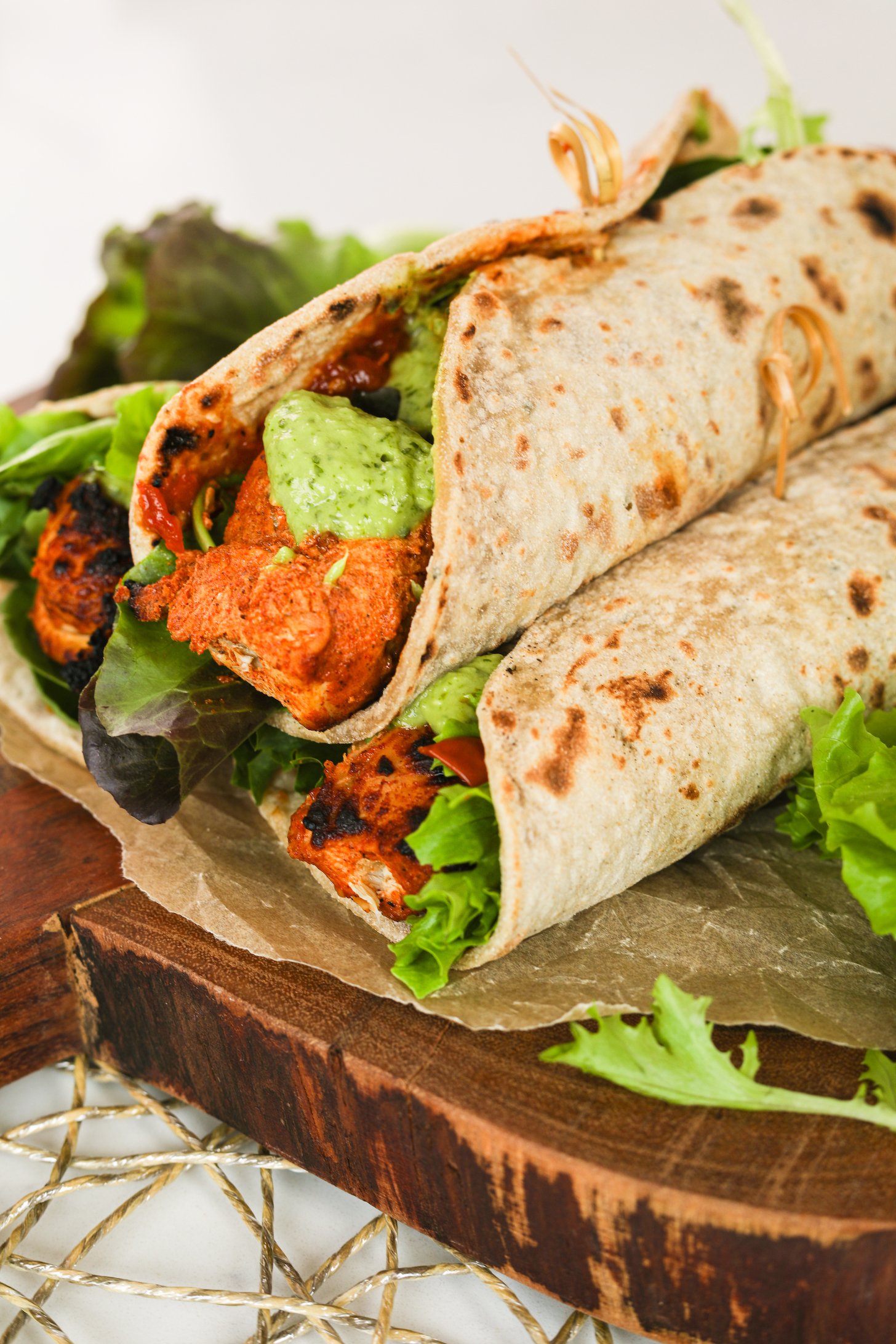 Perspective view of three chicken tikka wraps piled on top of fresh greens.