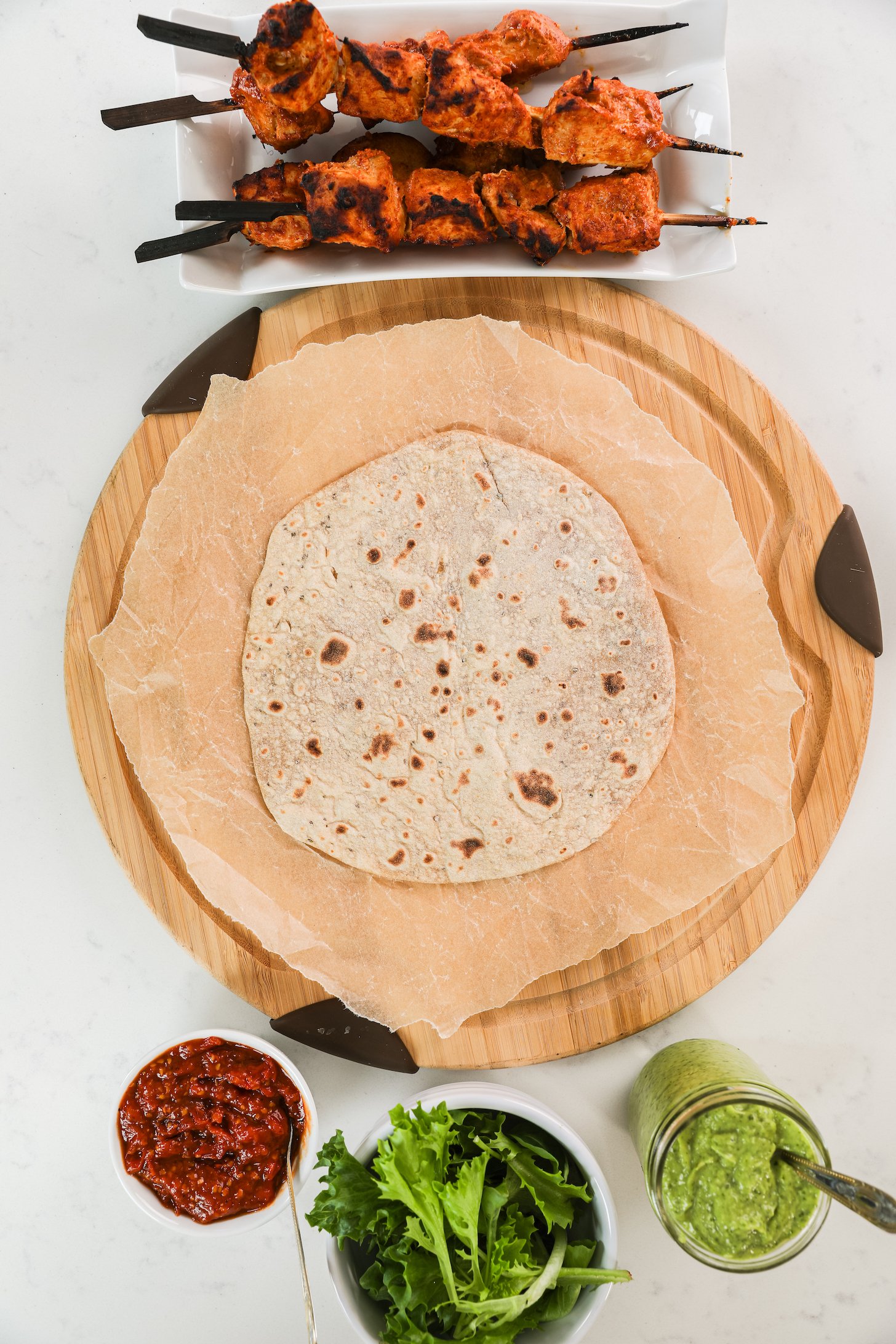 A roti with tandoori chicken skewers, sauces and salad greens nearby.