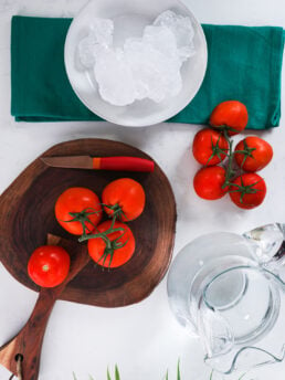 Tomatoes on a vine styled on a wooden board with a bowl of ice and a jug of water nearby.