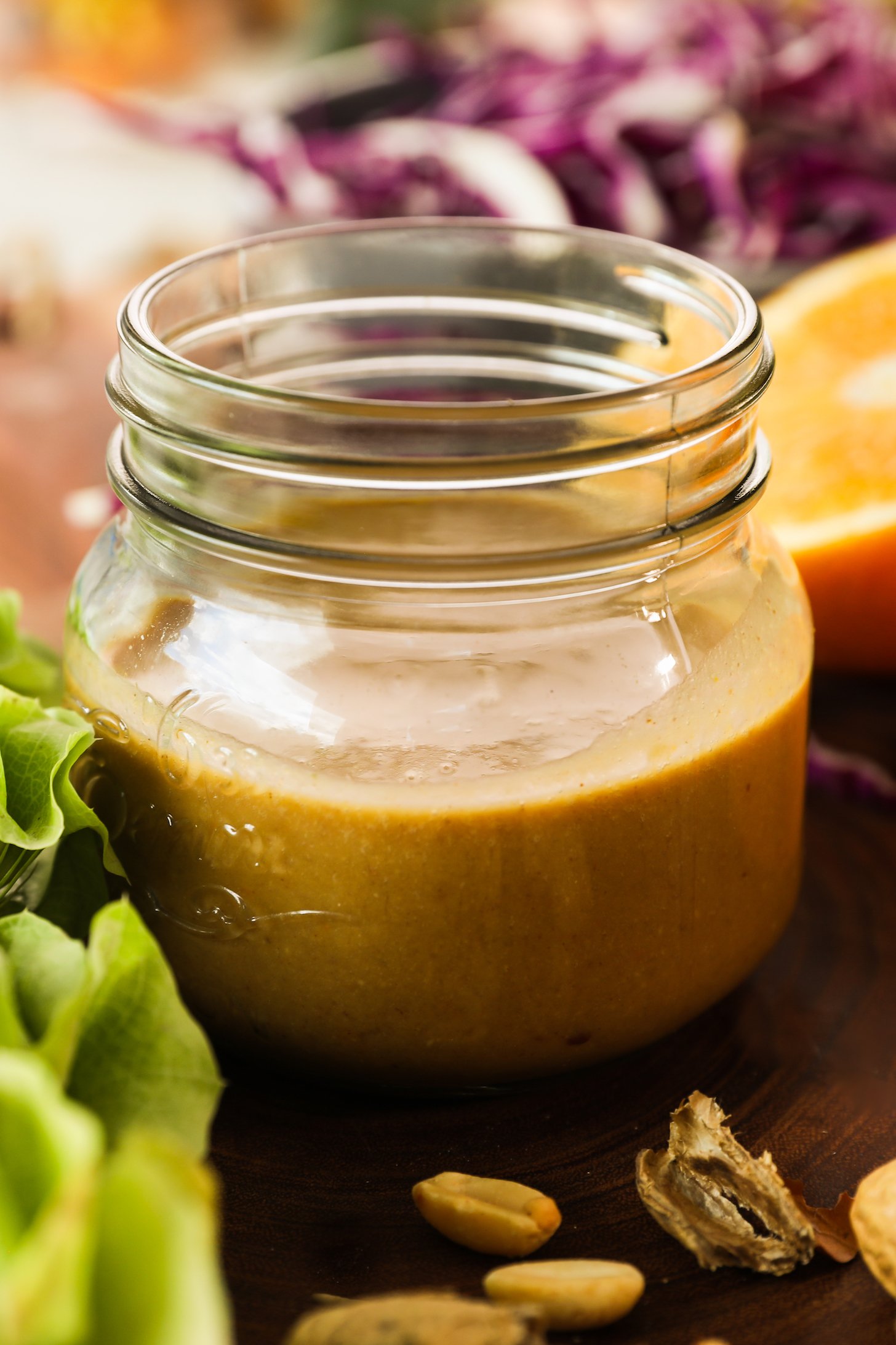 A small mason jar of brown dressing surrounded by colourful produce.