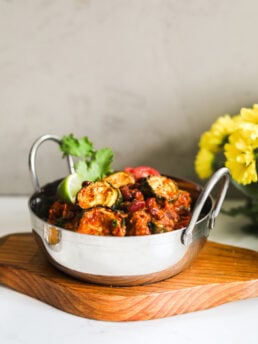 An Indian Karahi bowl of red kidney bean curry with zucchini styled with yellow flowers in the backgorund.