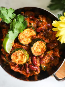 Flatlay image of a bowl of red kidney bean curry with zucchini topped with cilantro leaves and a wedge of lime.