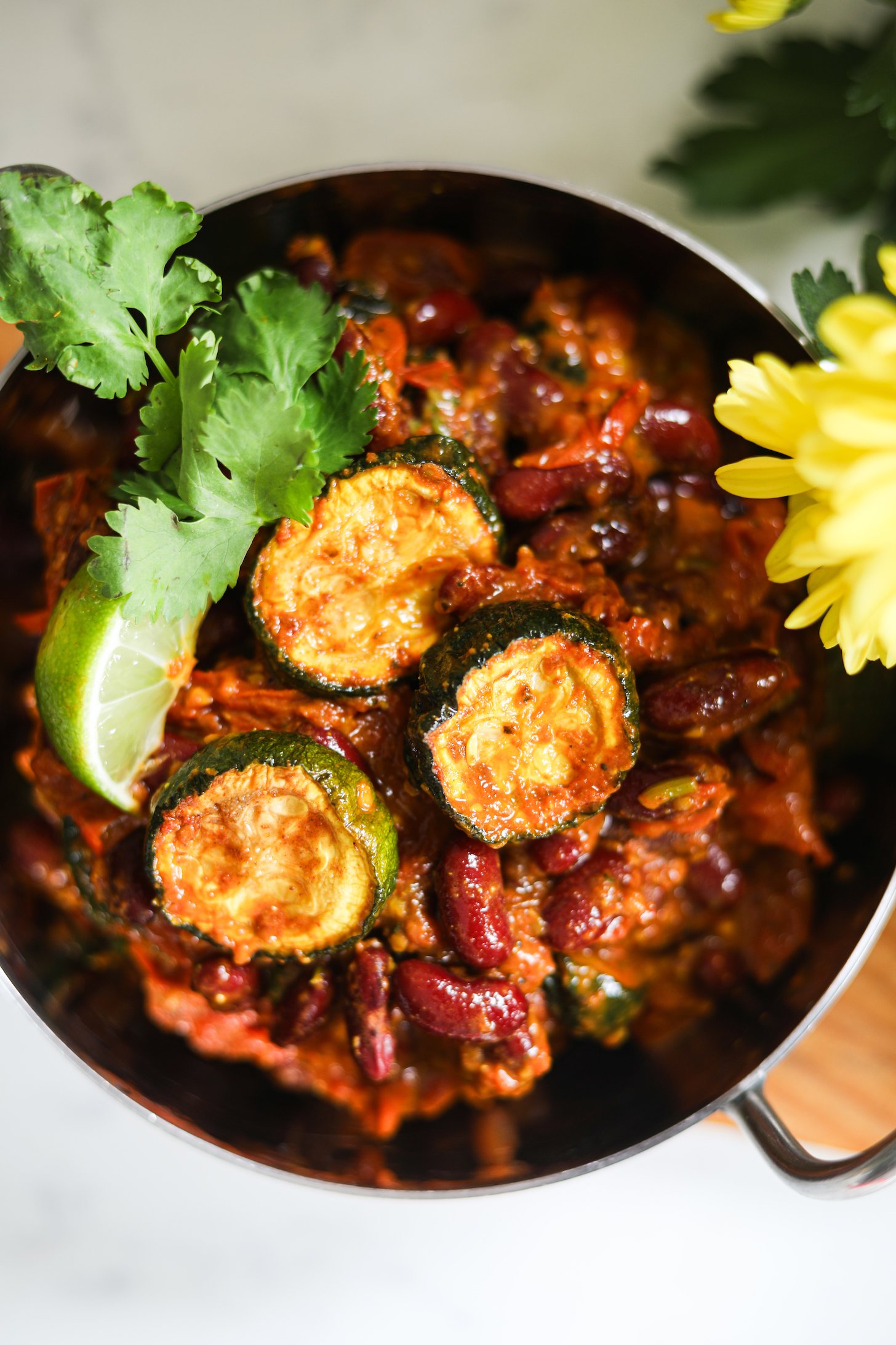 Flatlay image of a bowl of red kidney bean curry with zucchini topped with cilantro leaves and a wedge of lime.
