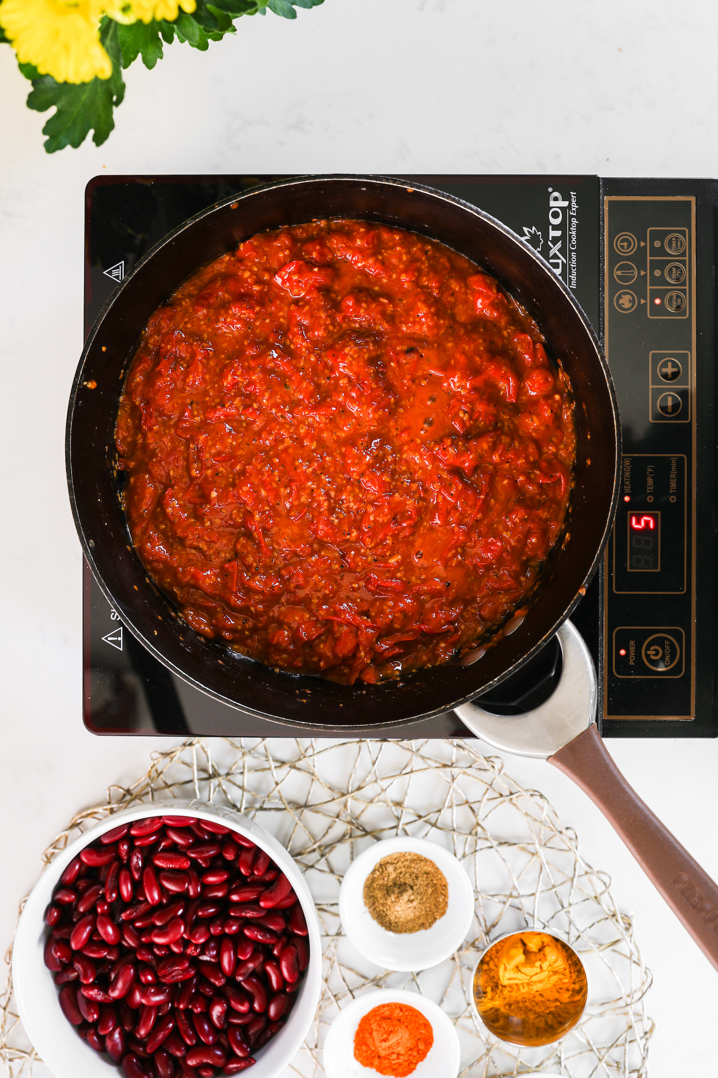 A pan of tomato sauce on a mobile cooktop with food ingredients close by.