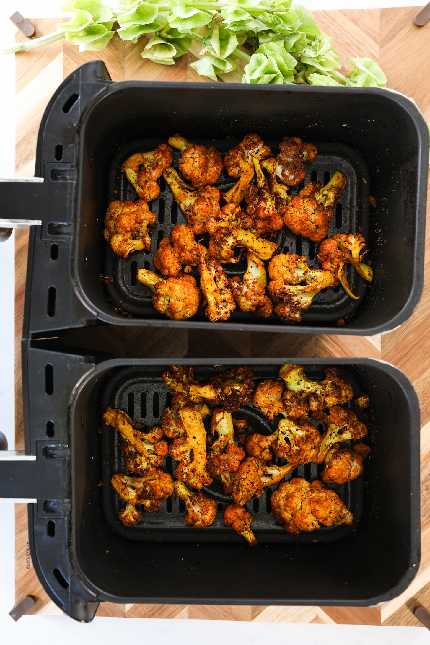 Two air fryer baskets of spice-coated cooked cauliflower bites.