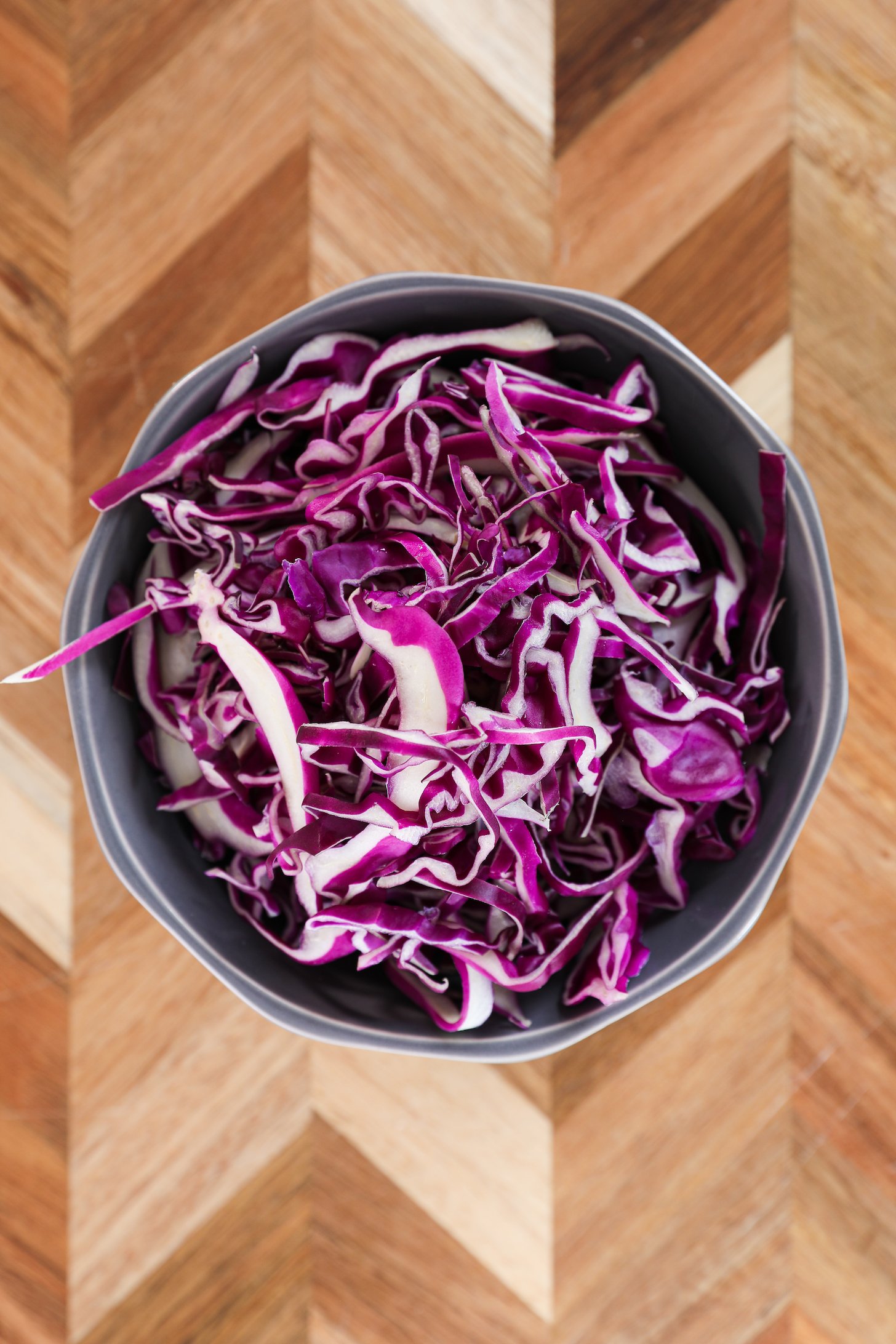 A bowl of shredded red cabbage on a wooden board.