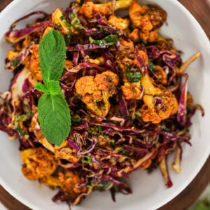 Top view of a bowl of spiced cauliflower and shredded red cabbage mix topped with a sprig of mint.
