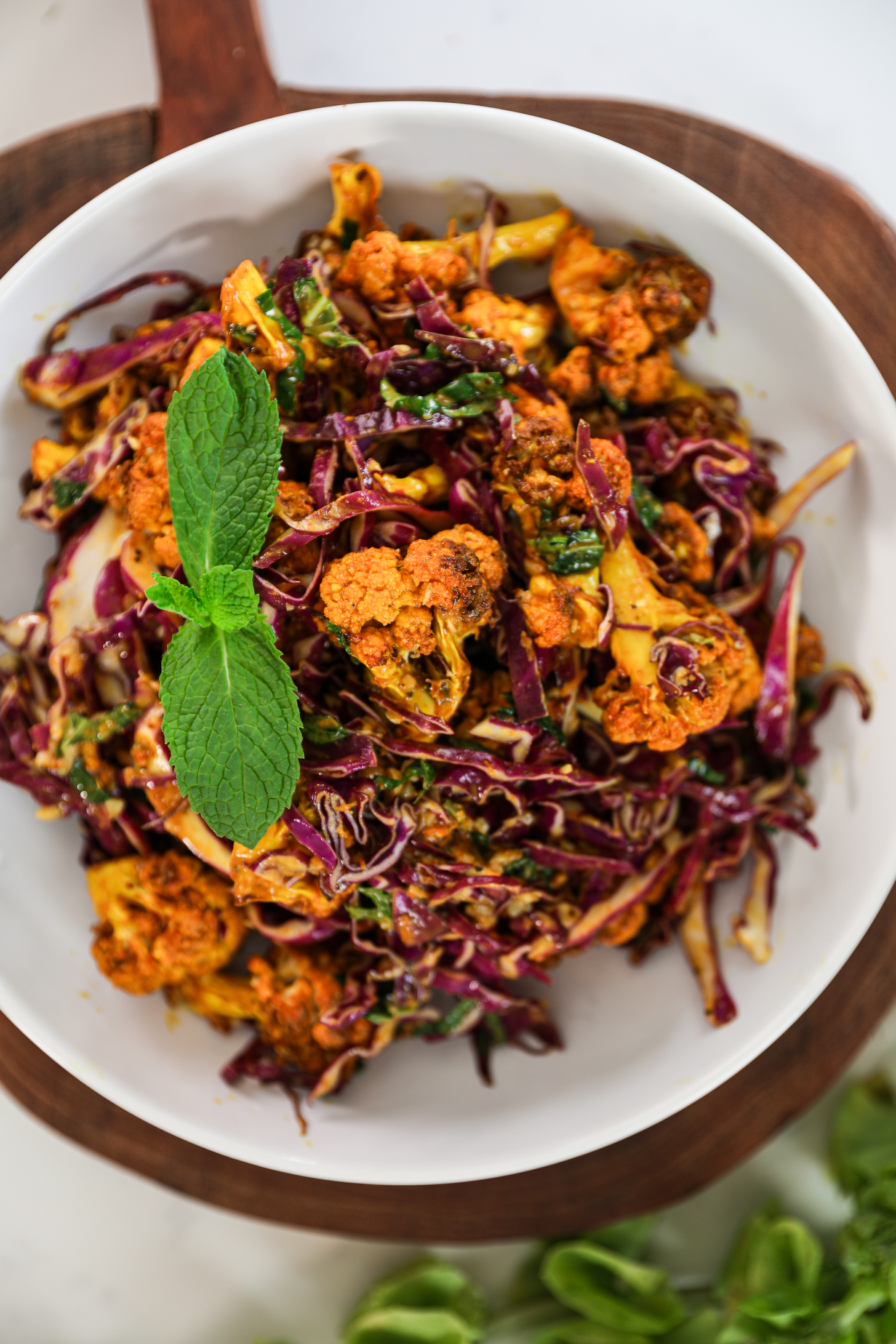 Top view of a bowl of spiced cauliflower and shredded red cabbage mix topped with a sprig of mint.