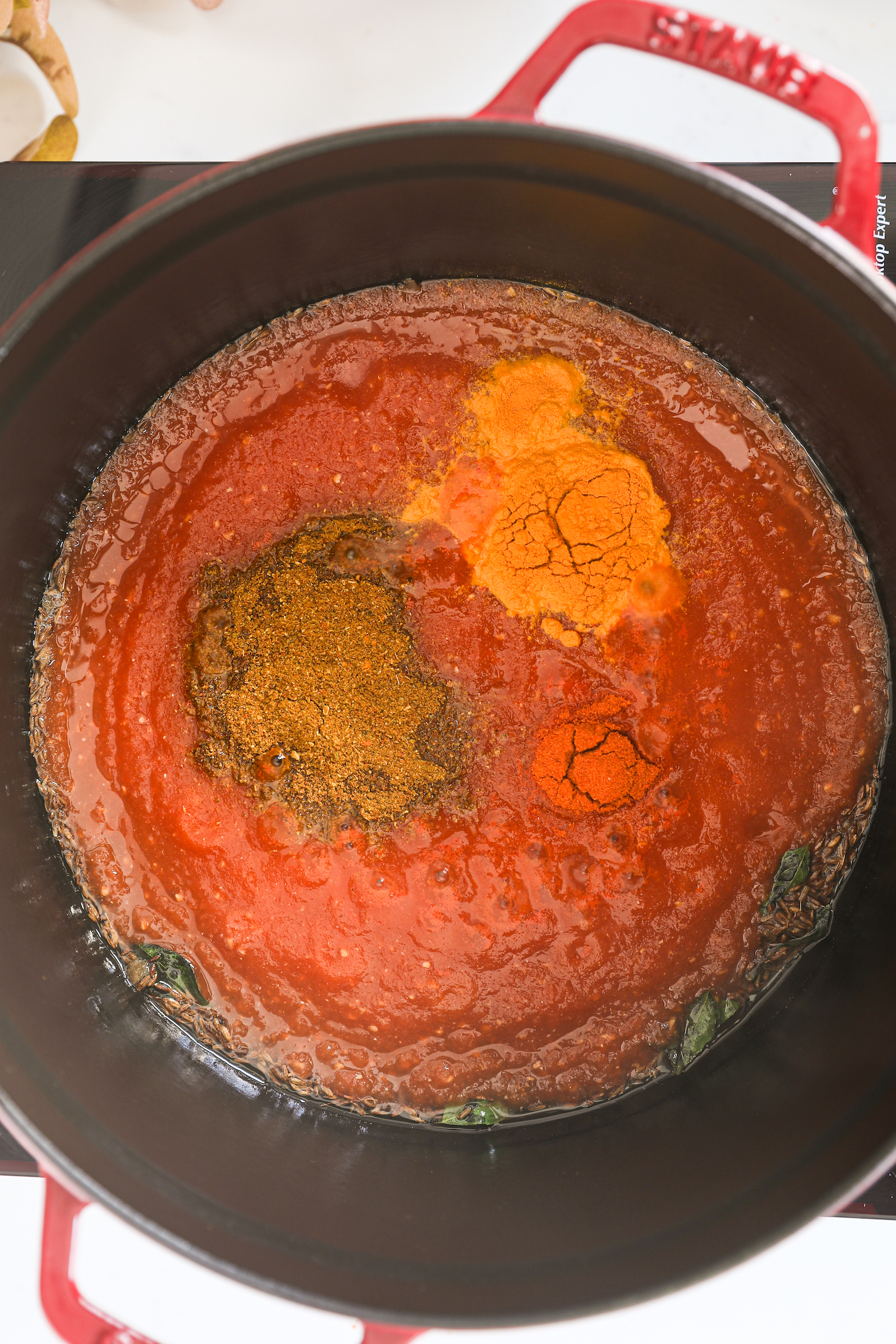 A cast iron pot with tomato sauce that's topped with spices.