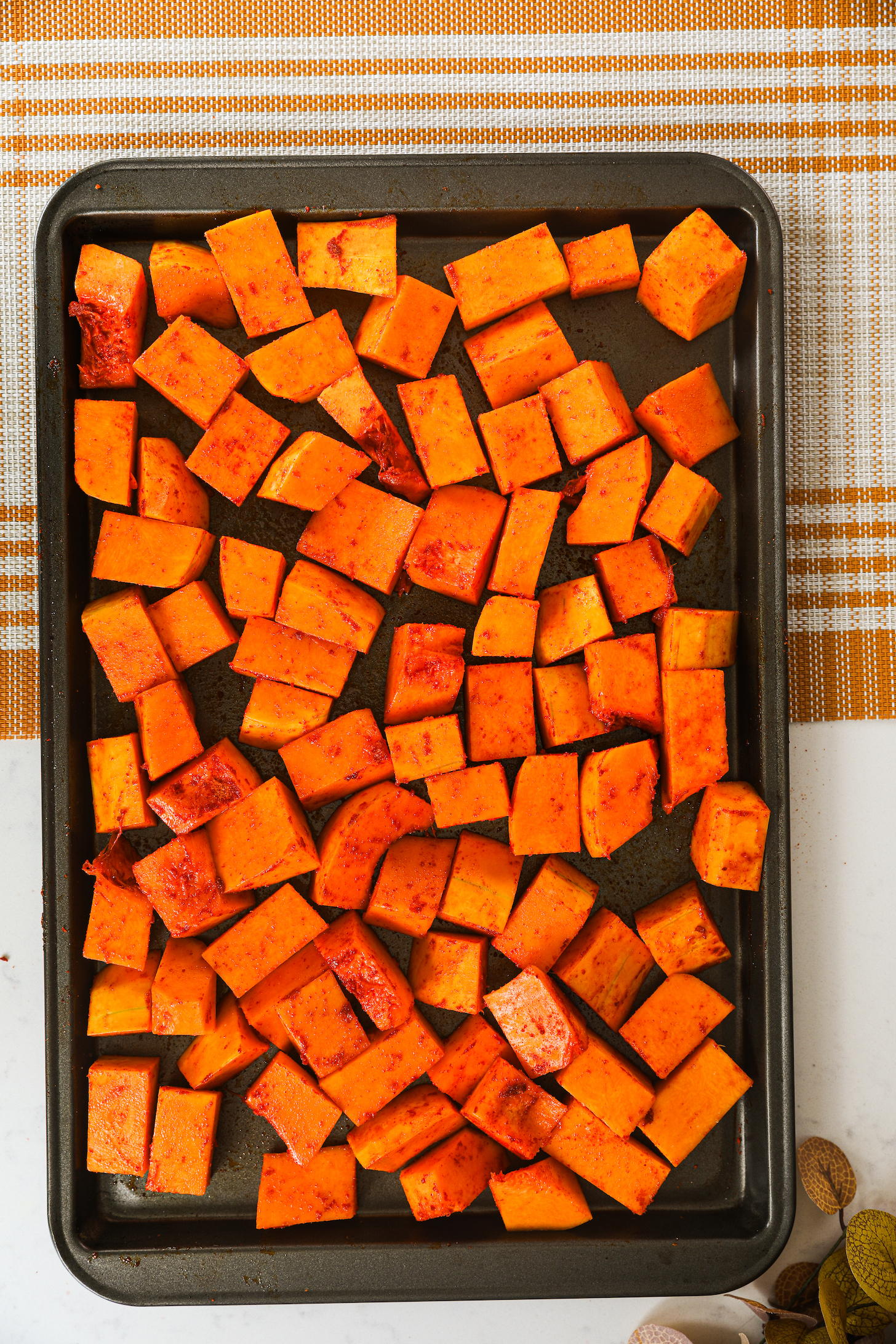 Butternut squash chunks neatly lined up in a single row on an oven tray.